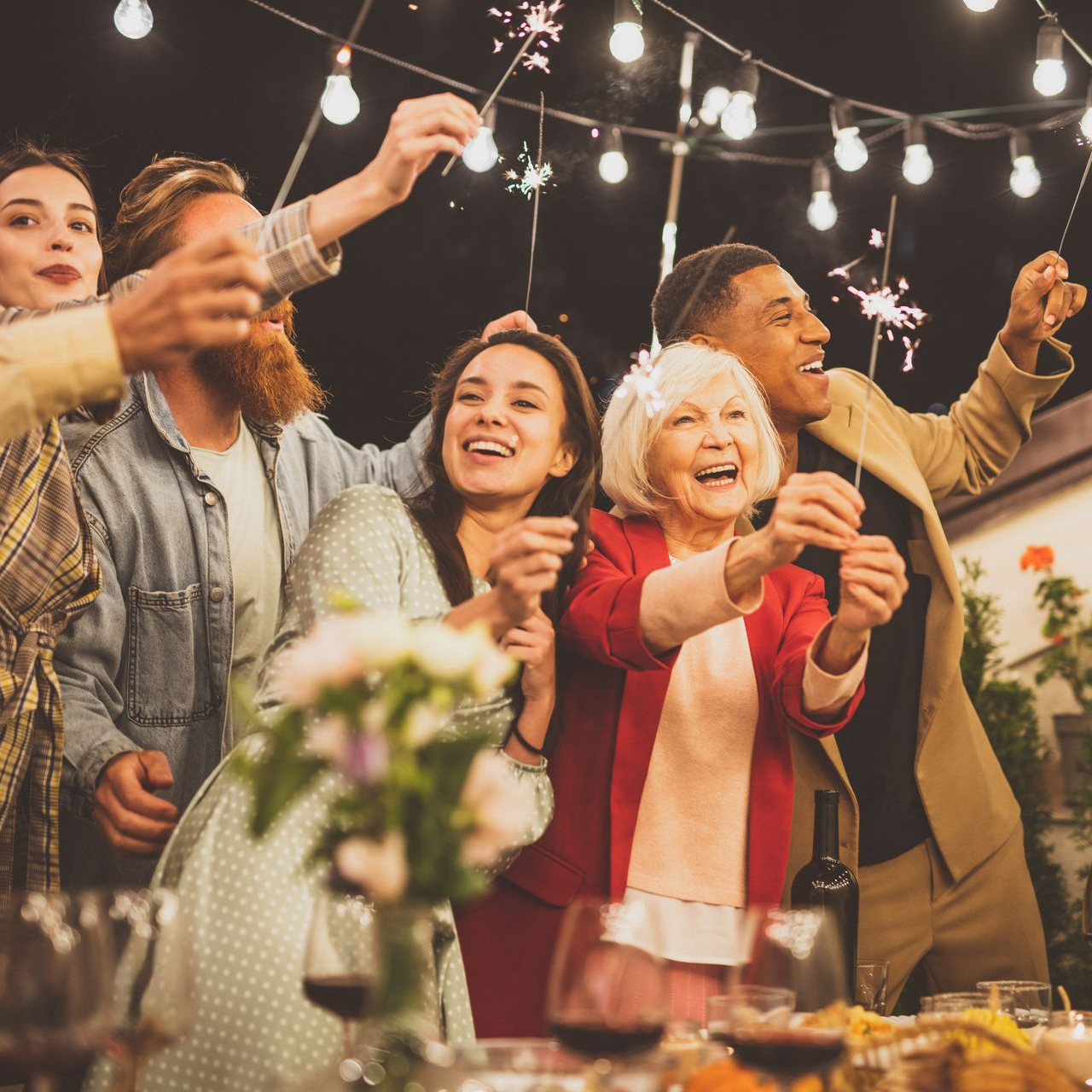 Des gens célèbrent en plein air avec des feux de Bengale et des guirlandes lumineuses.