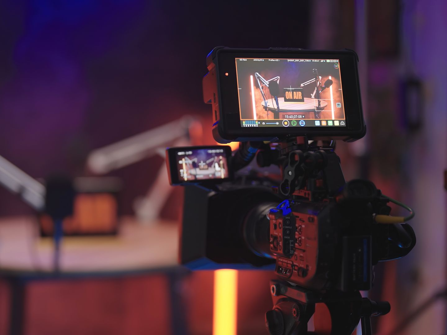 Une caméra vidéo avec deux écrans affichant un décor de scène baigné de lumière rouge et violette.