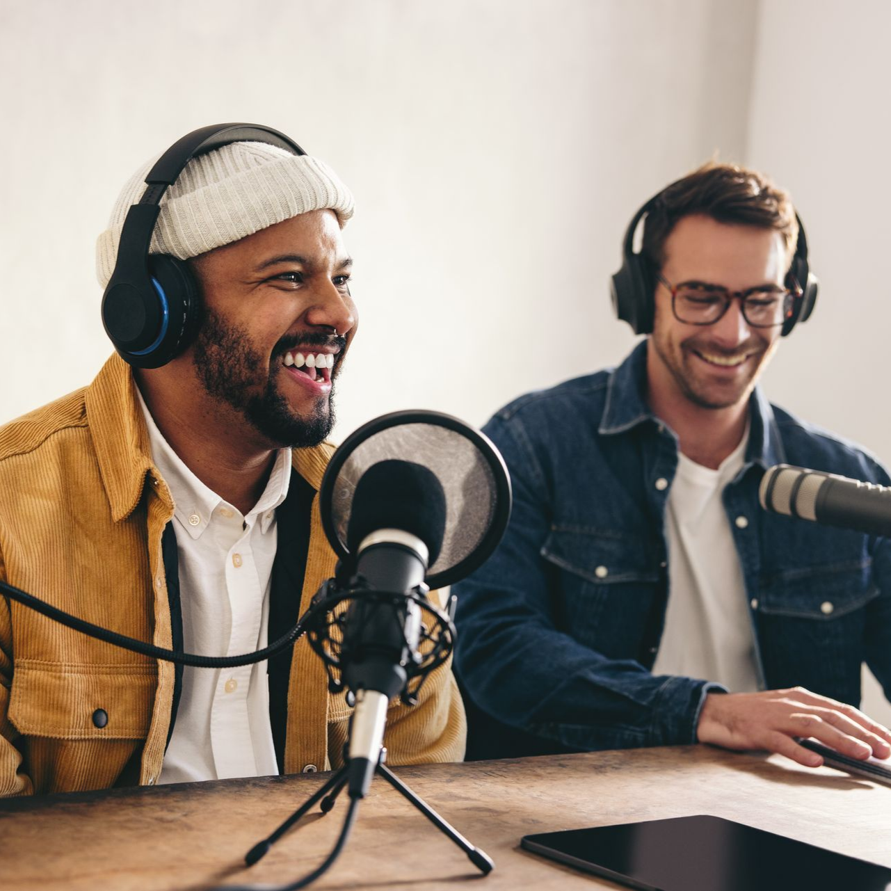 Deux personnes souriantes, portant des écouteurs, enregistrent un podcast à une table équipée de microphones.