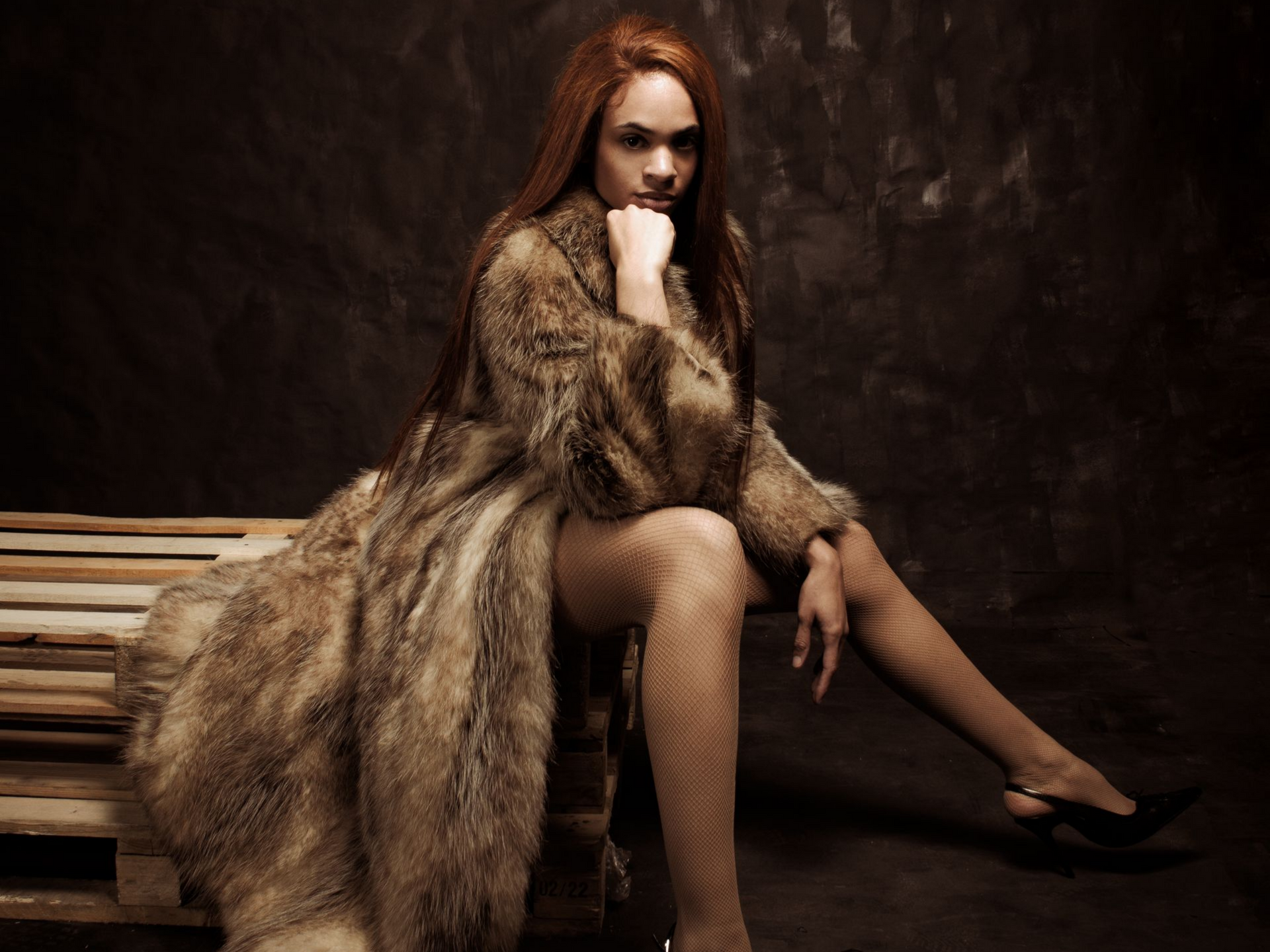 Une femme en manteau de fourrure est assise sur des palettes en bois et regarde l'objectif.