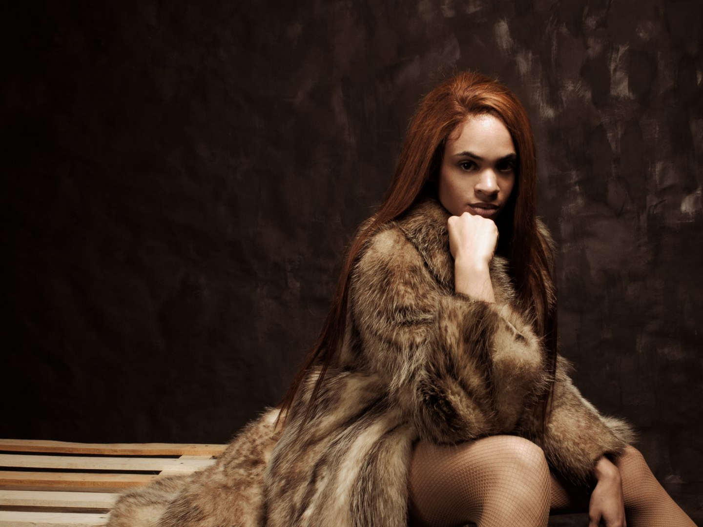 Femme aux cheveux roux, vêtue d'un manteau de fourrure, assise sur un banc en bois, sur fond sombre.