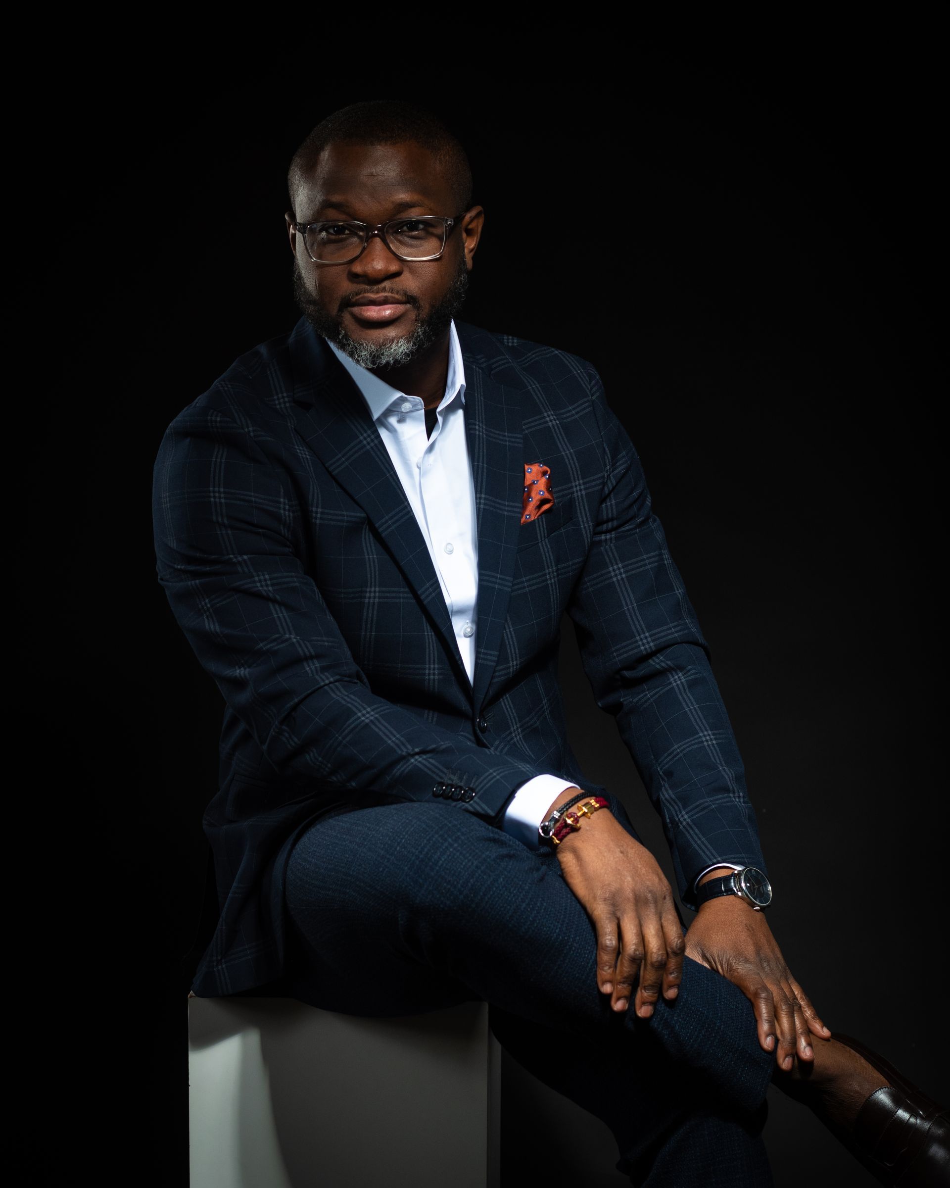 Homme en costume bleu marine, souriant, regardant sur le côté, la main sur le menton. Intérieur lumineux.