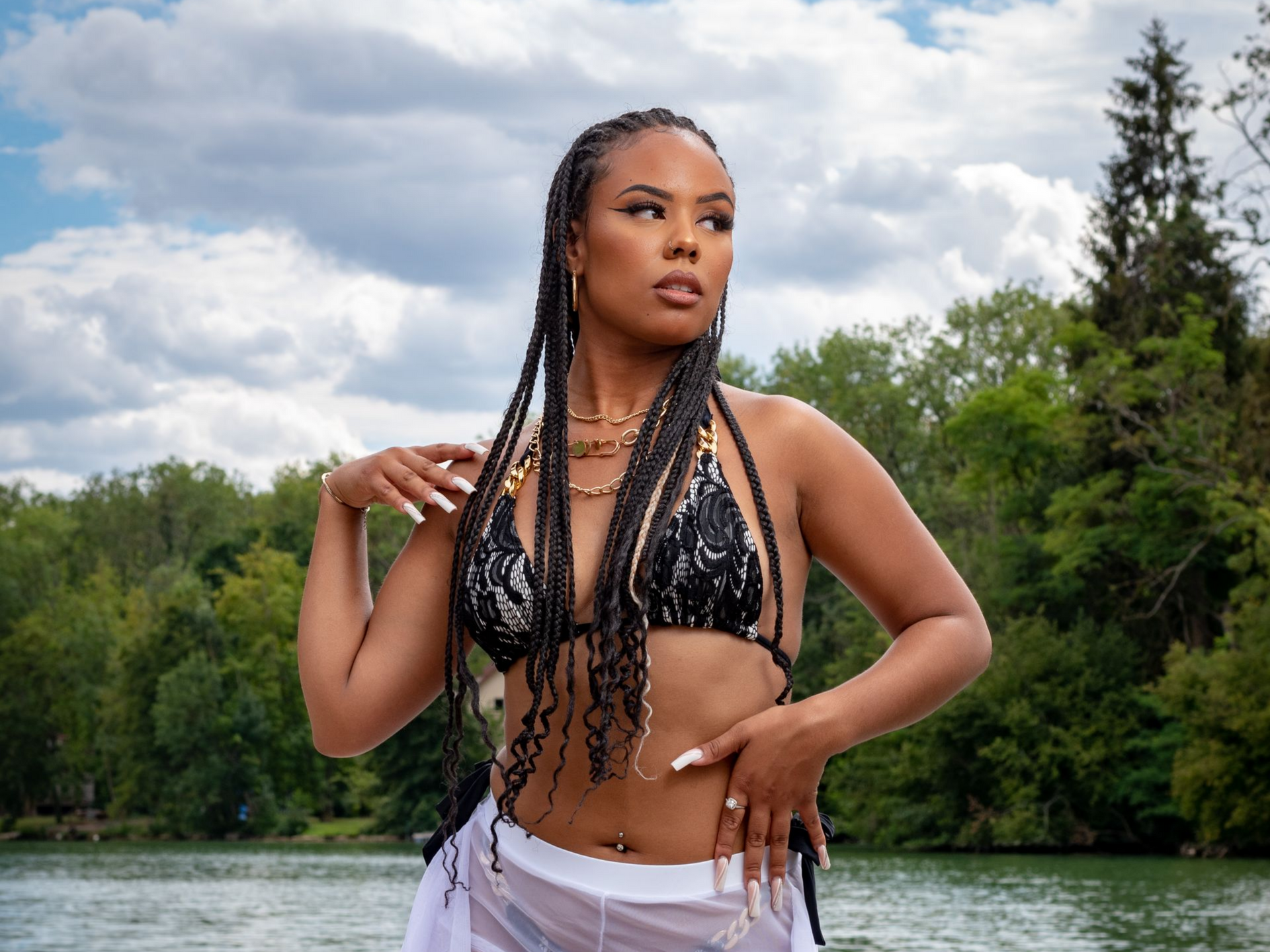 Femme en haut de bikini noir et jupe blanche près de l'eau, regardant sur le côté.