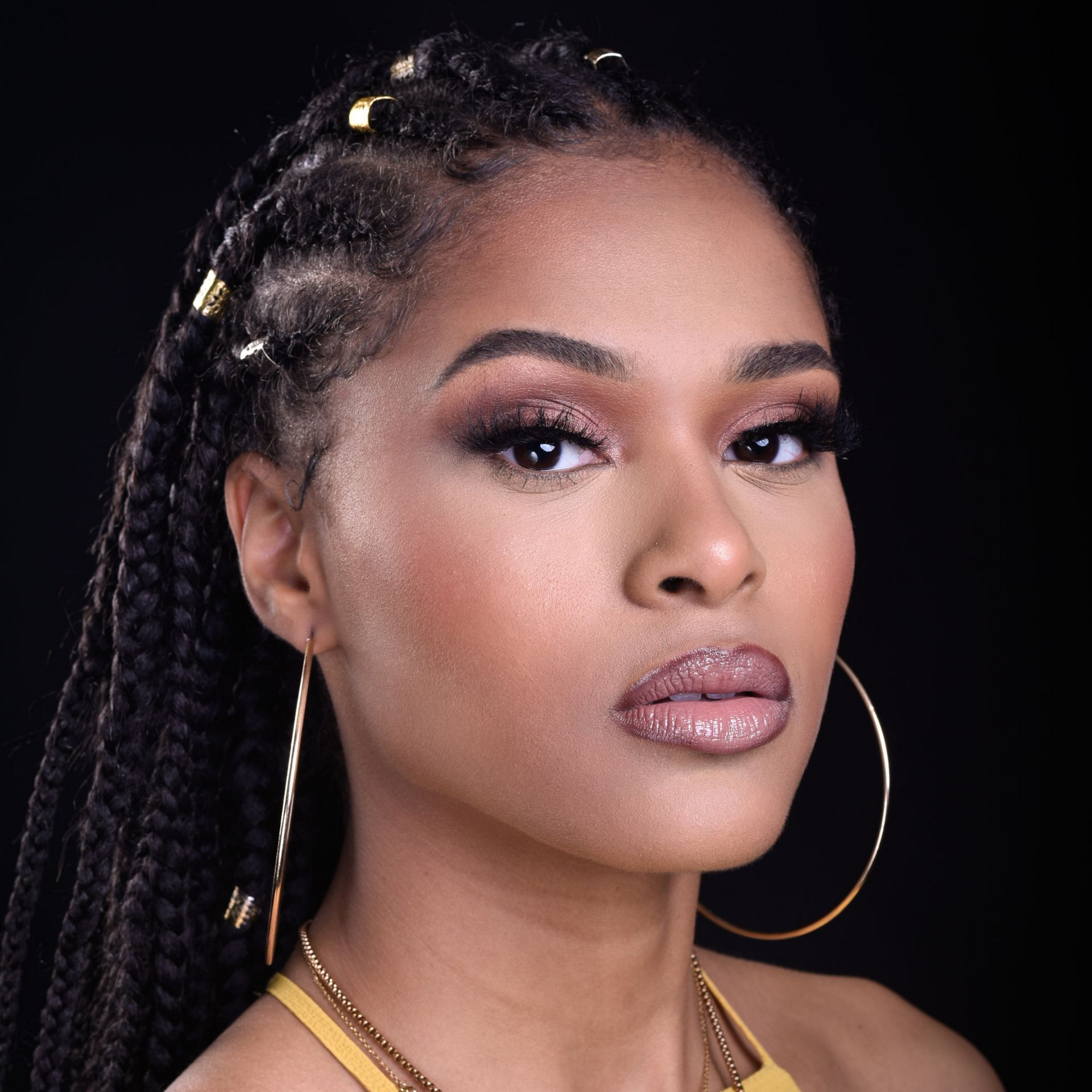 Femme avec des tresses, des créoles et un maquillage glamour.