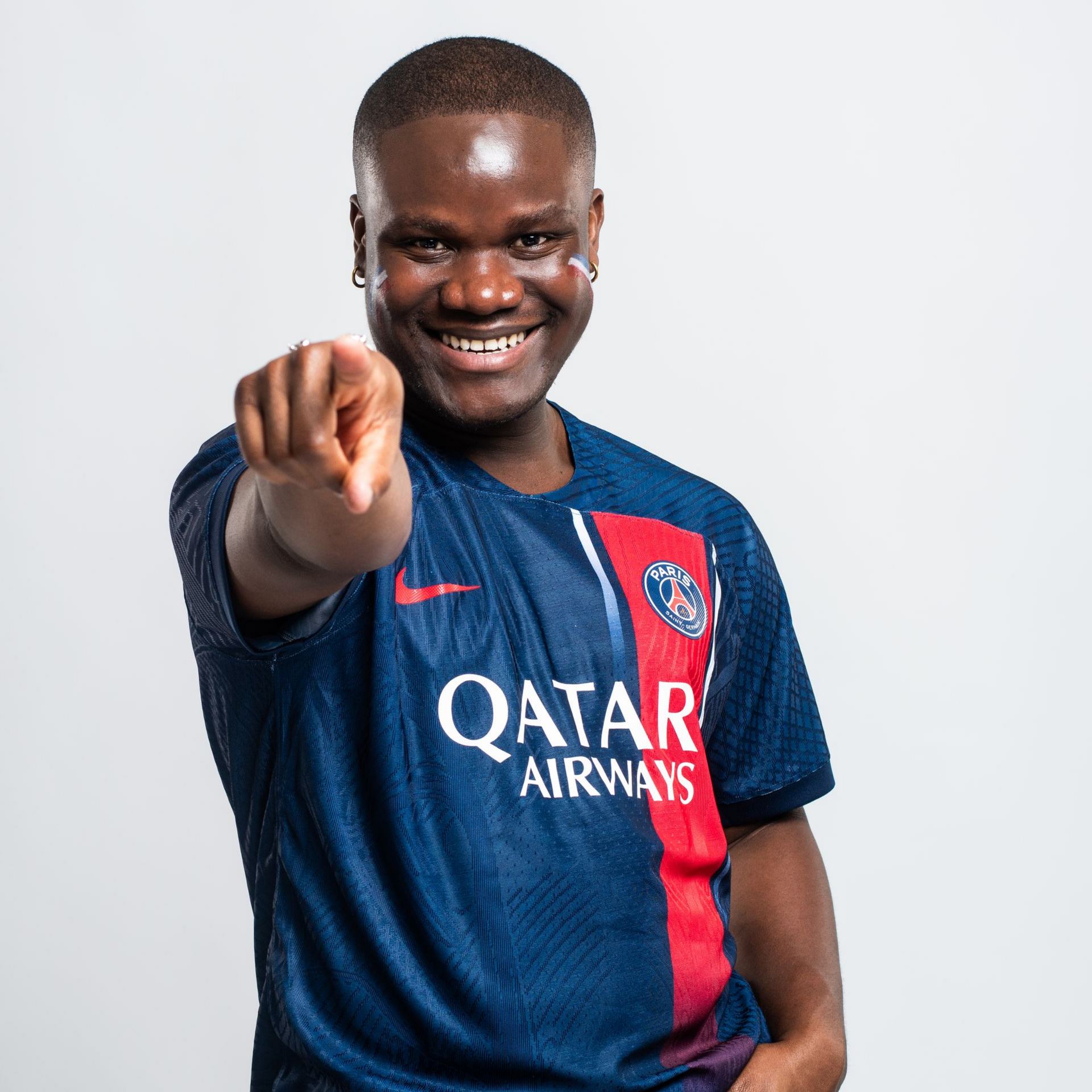 Homme en maillot bleu du PSG, souriant et pointant du doigt le spectateur.