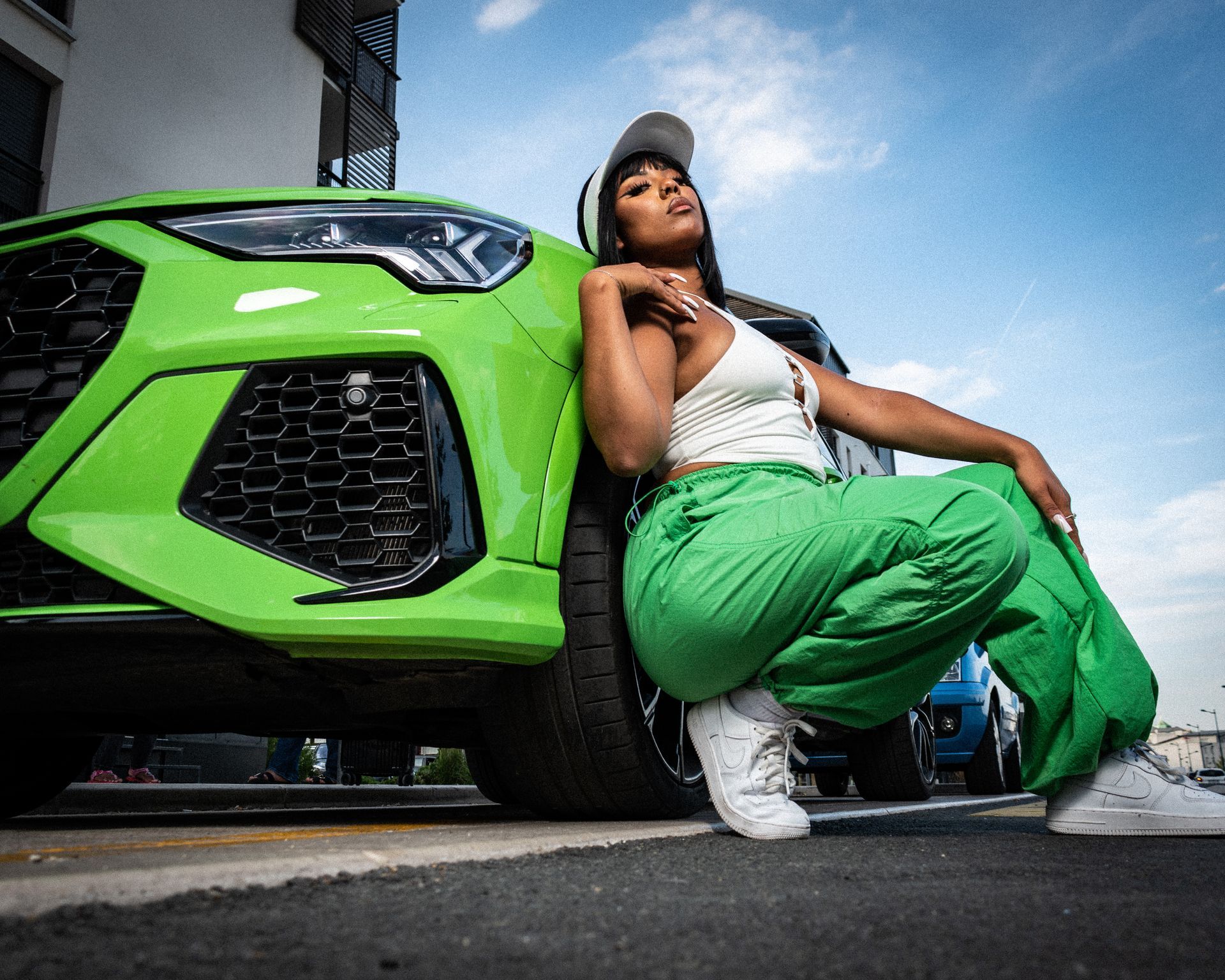 Femme en tenue verte posant à côté d'une voiture vert vif, en extérieur.