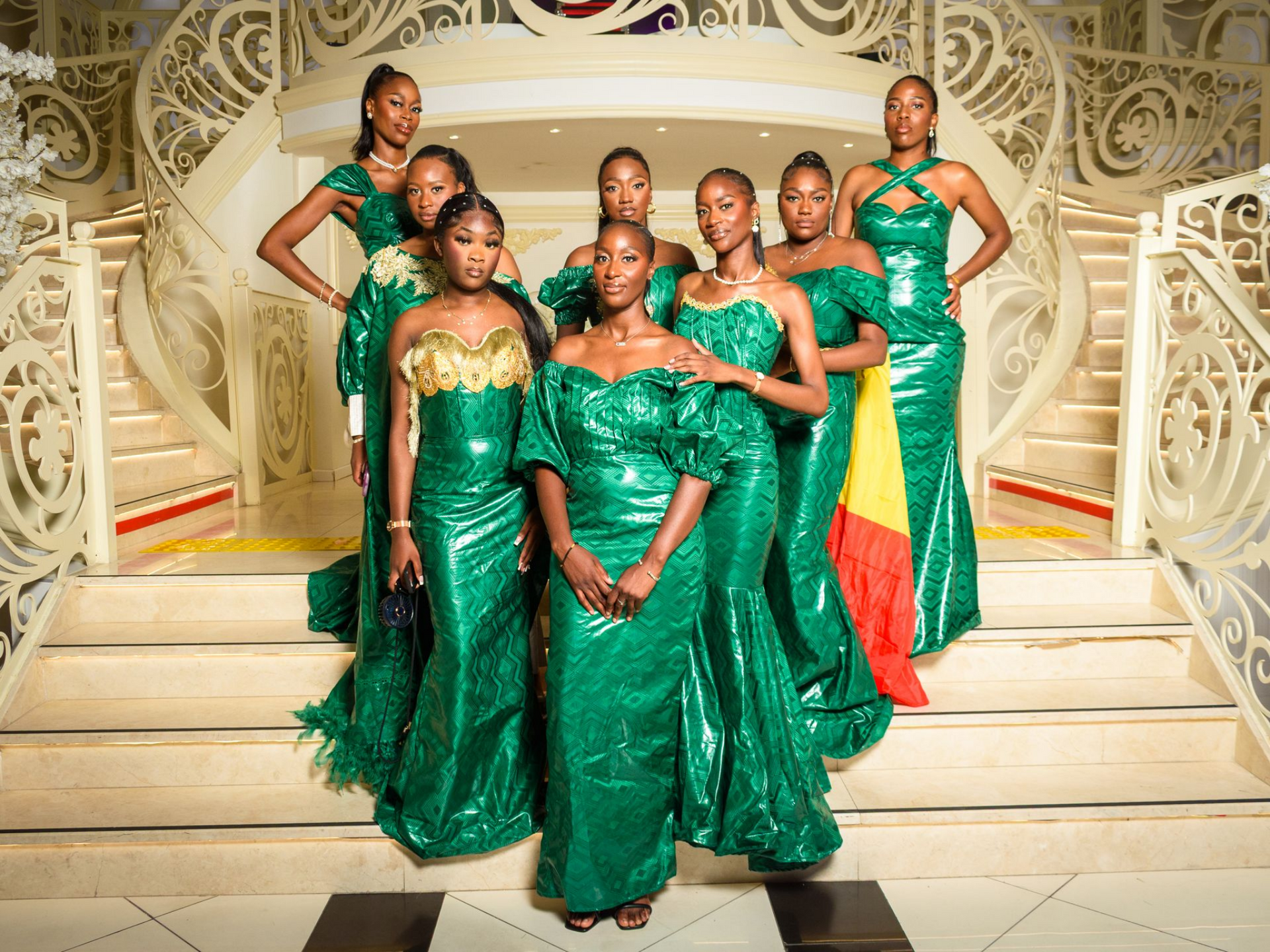 Un groupe de femmes en robes vertes pose sur un escalier à la rampe ornée.