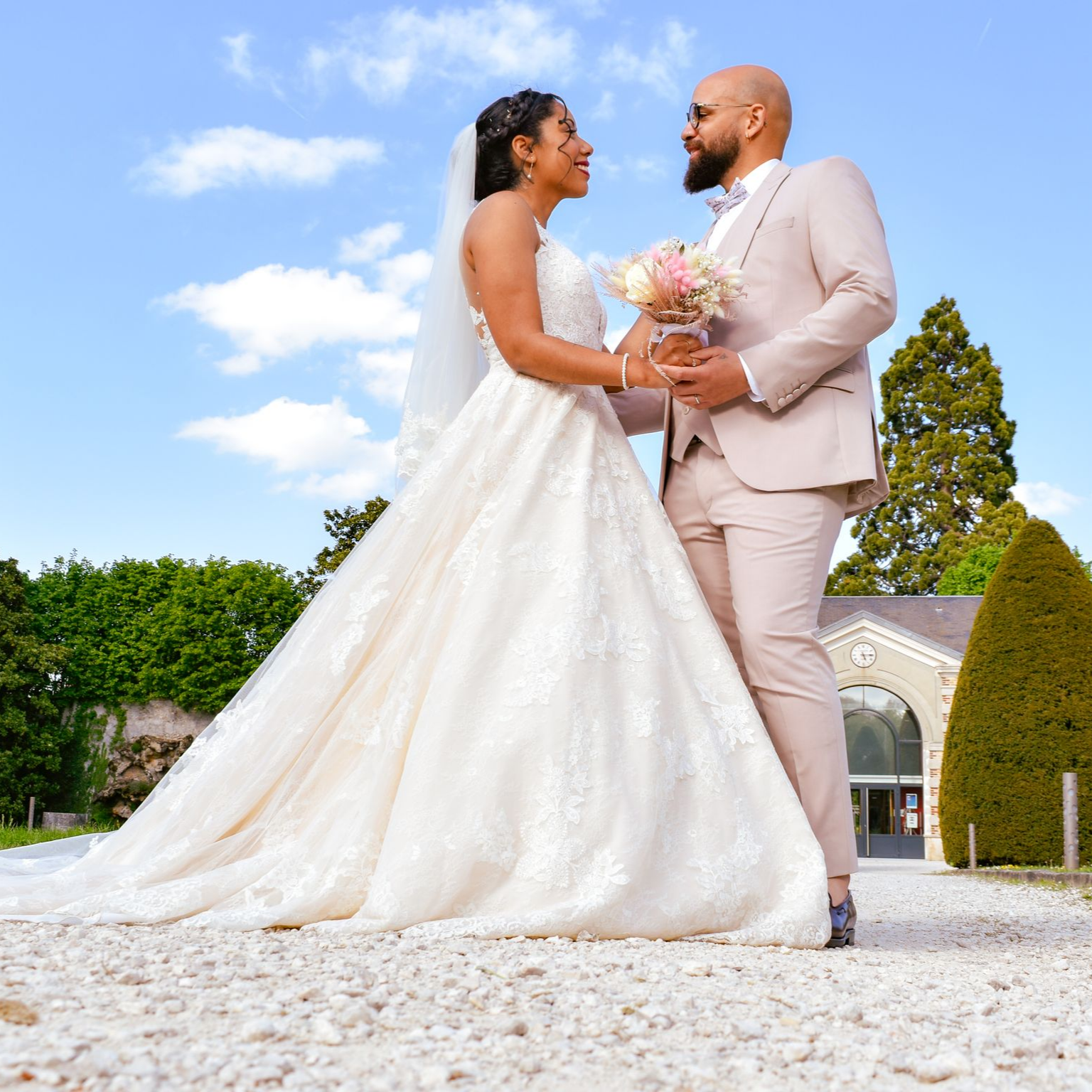 Le jour de leur mariage, les mariés se regardent avec amour. Elle porte une robe blanche et tient un bouquet. Il porte un costume rose.