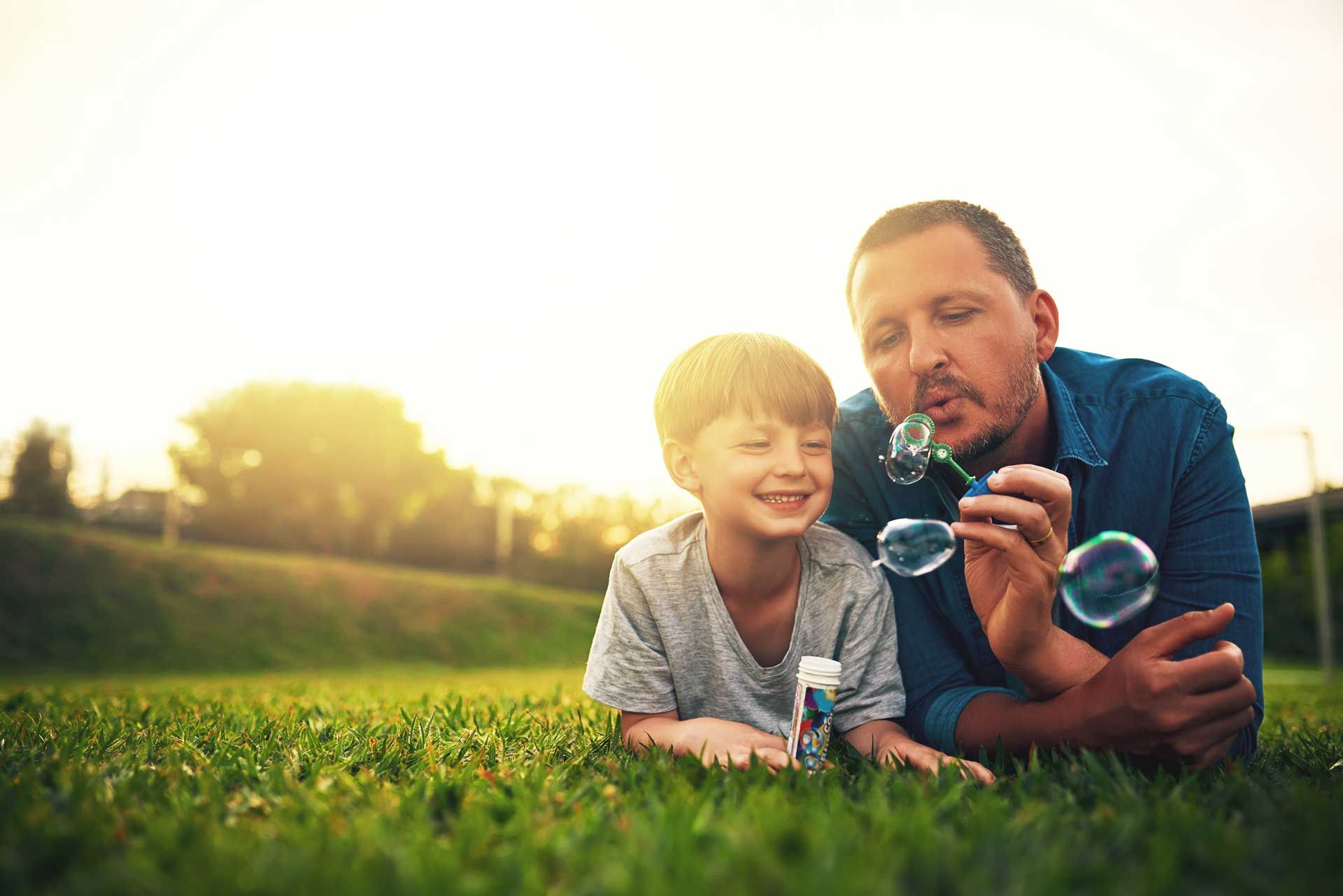 Un père et son fils allongés dans l'herbe soufflant des bulles de savon