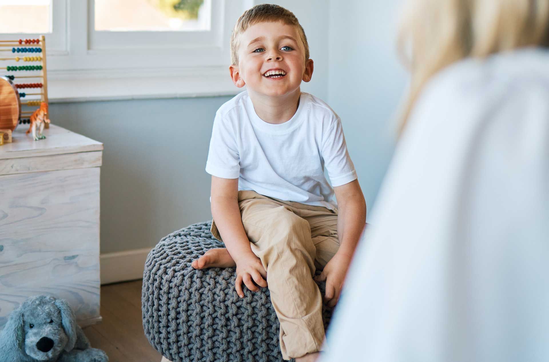 Un enfant assis dans sa chambre souriant à une personne vue de dos