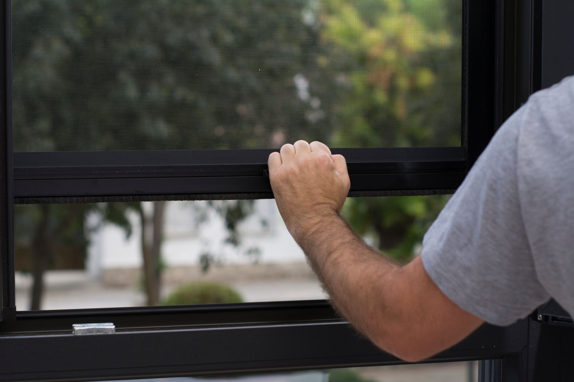 Un homme ferme une moustiquaire accrochée à une fenêtre