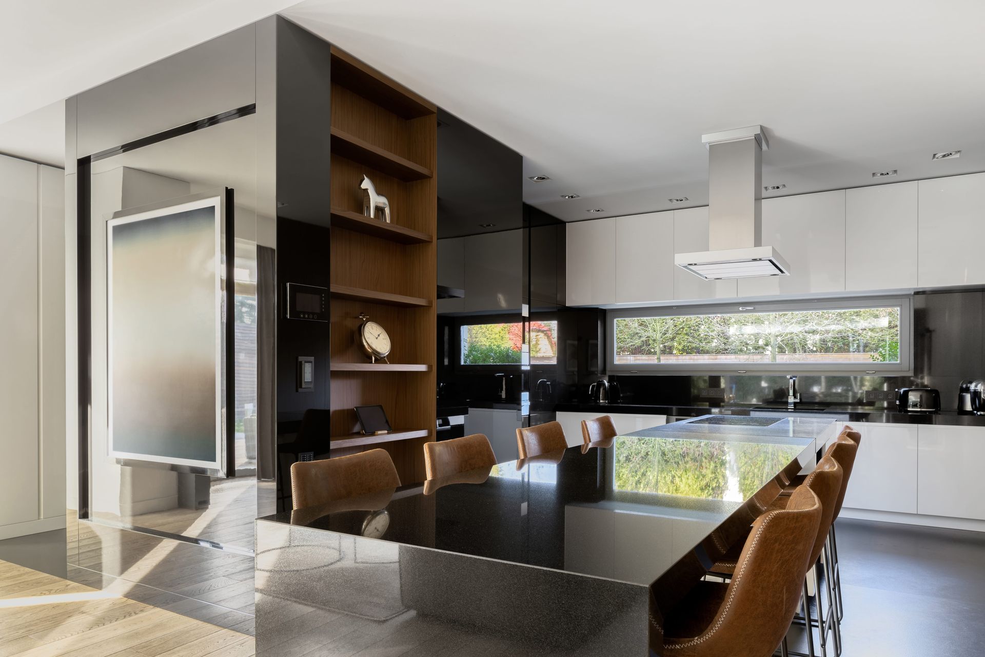 Cocina moderna con mesa de comedor negra brillante, sillas marrones y grandes ventanales con vistas a la vegetación.