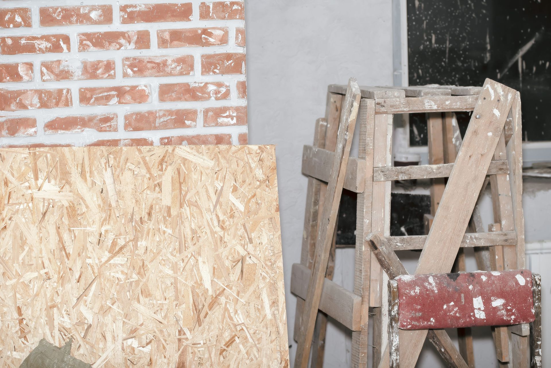 Tablero OSB y escaleras desgastadas apoyadas contra una pared de ladrillo y estuco en construcción.