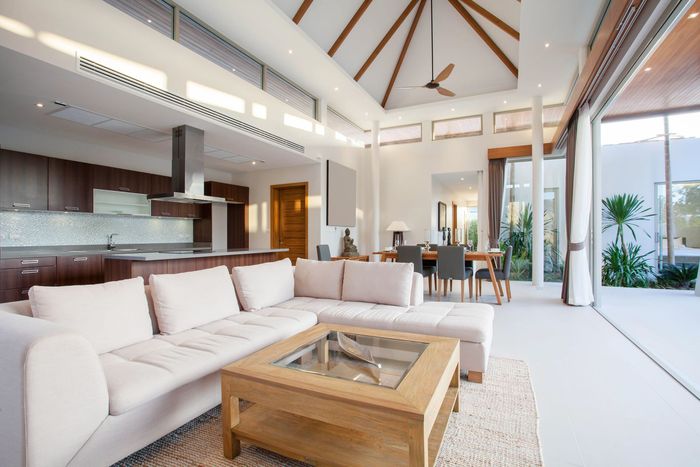 Salón luminoso y moderno con sofás blancos, mesa de centro de madera, techos altos y grandes puertas de cristal.
