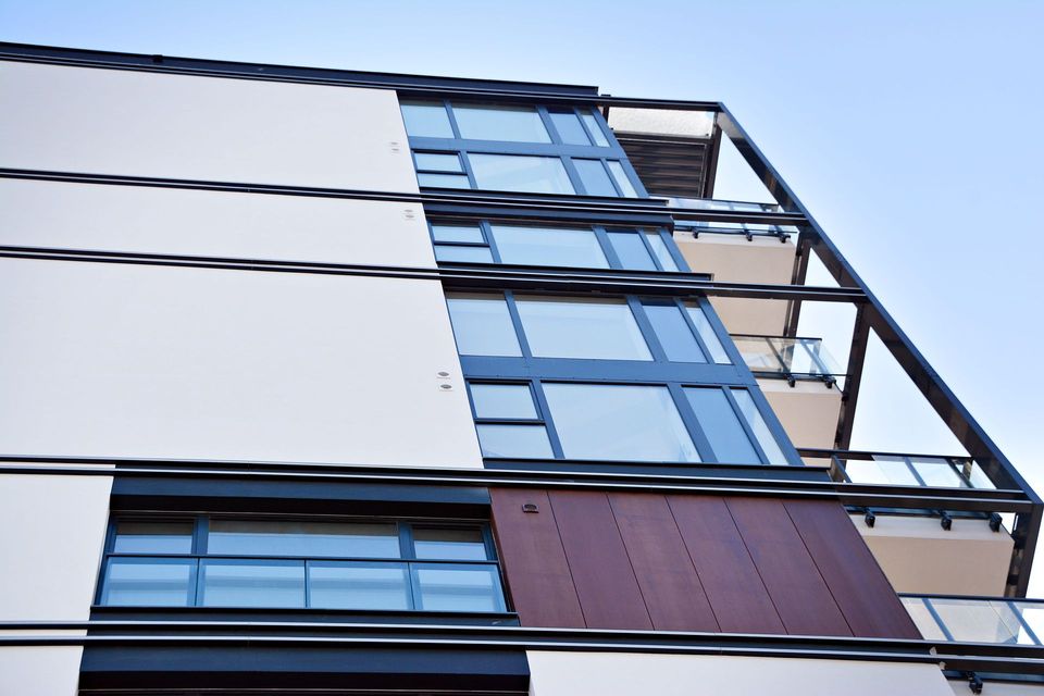 Fachada de edificio moderno con paneles blancos, ventanas de vidrio azul y una sección decorativa marrón.