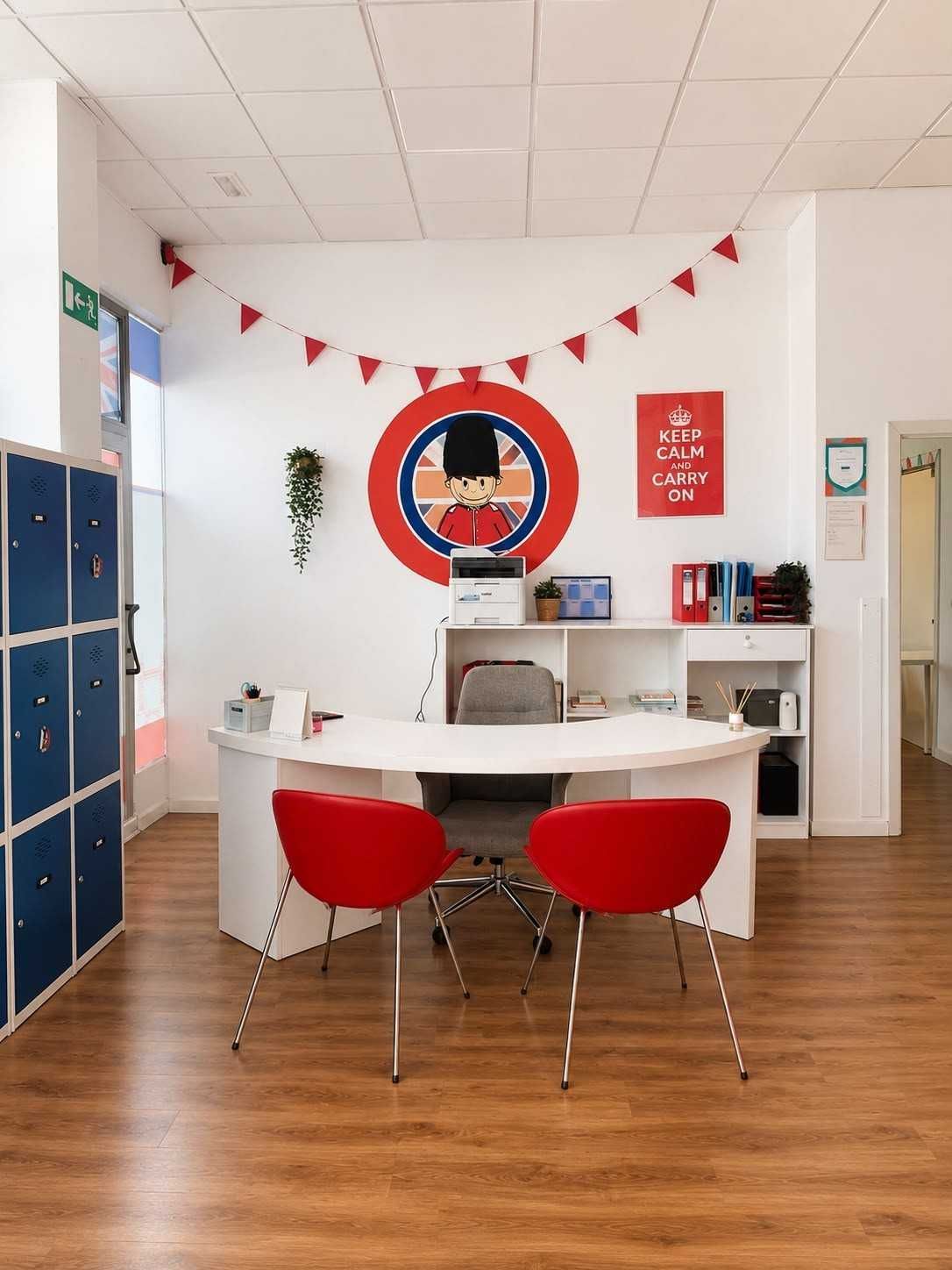 Acogedora sala de estar de oficina con sillas rojas, mesa redonda, taquillas azules y guirnaldas rojas en la pared.