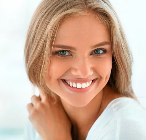Un primer plano de una mujer sonriendo con la mano en el cuello.