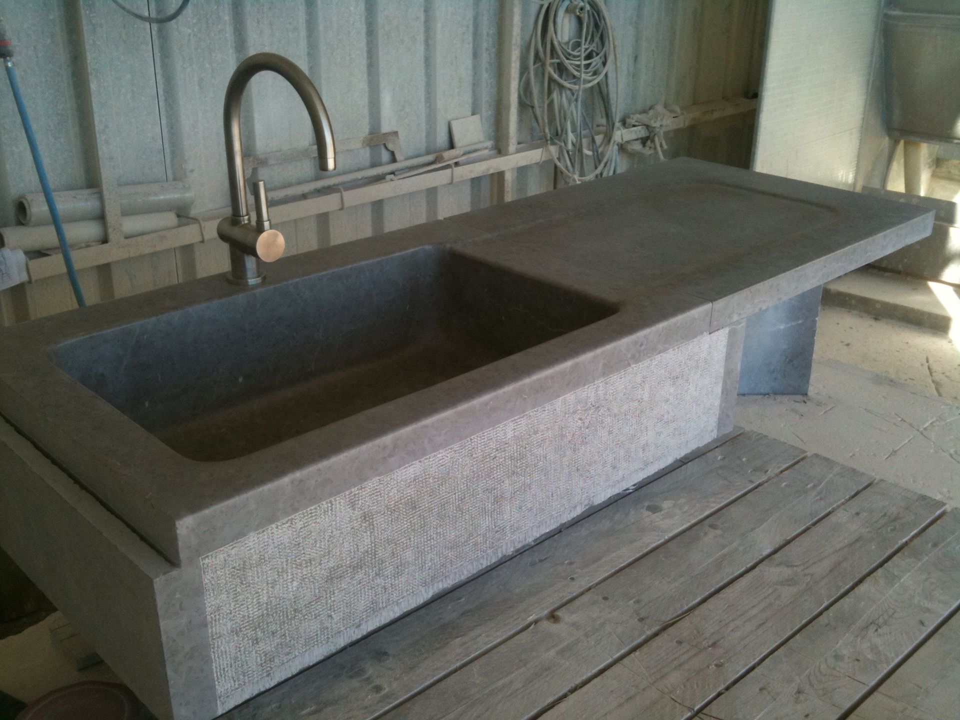 Évier en pierre avec robinet sur une base en béton, posé sur des planches de bois.