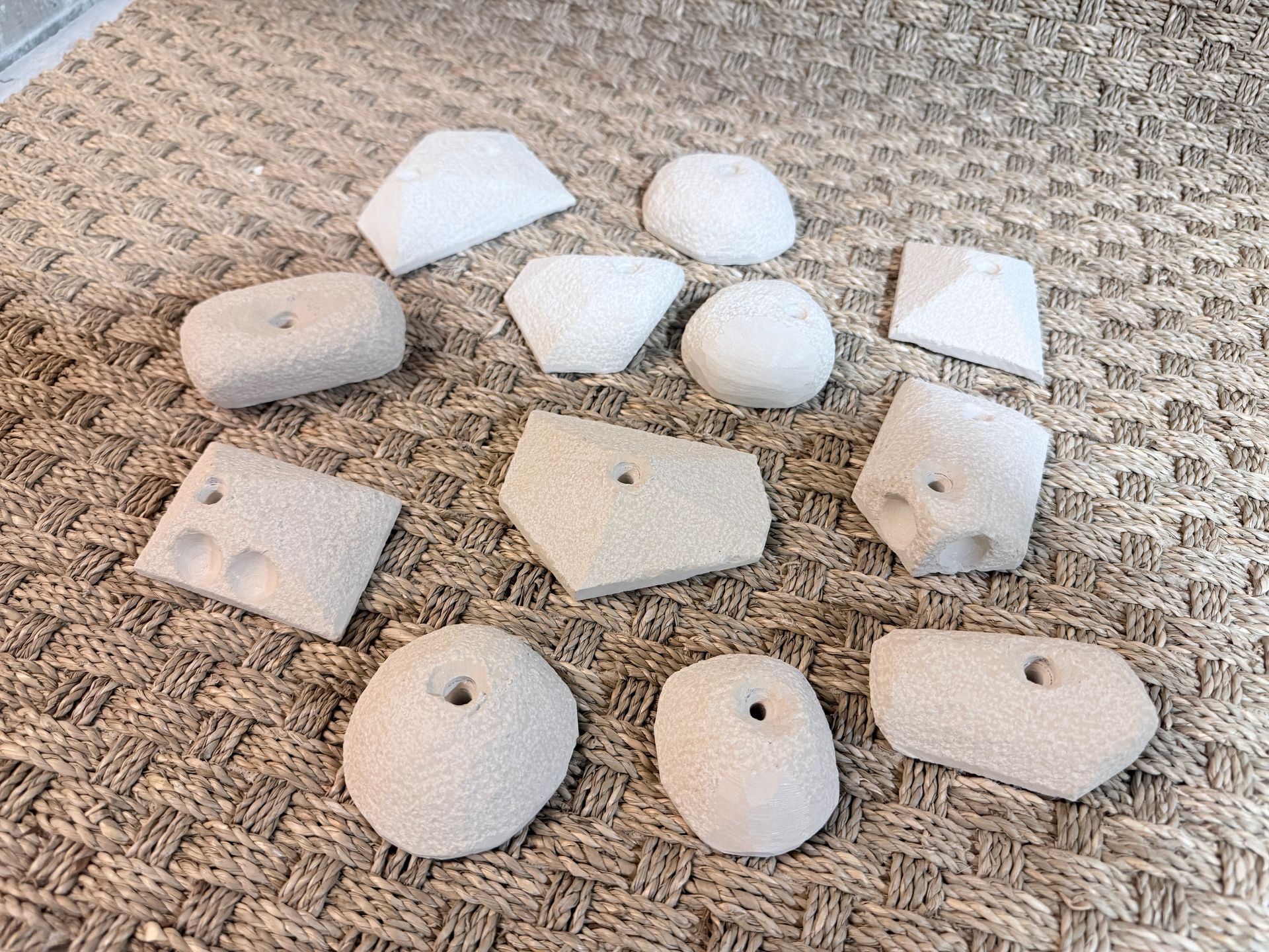 Assortiment de prises d'escalade blanches et géométriques sur une surface texturée de couleur neutre.