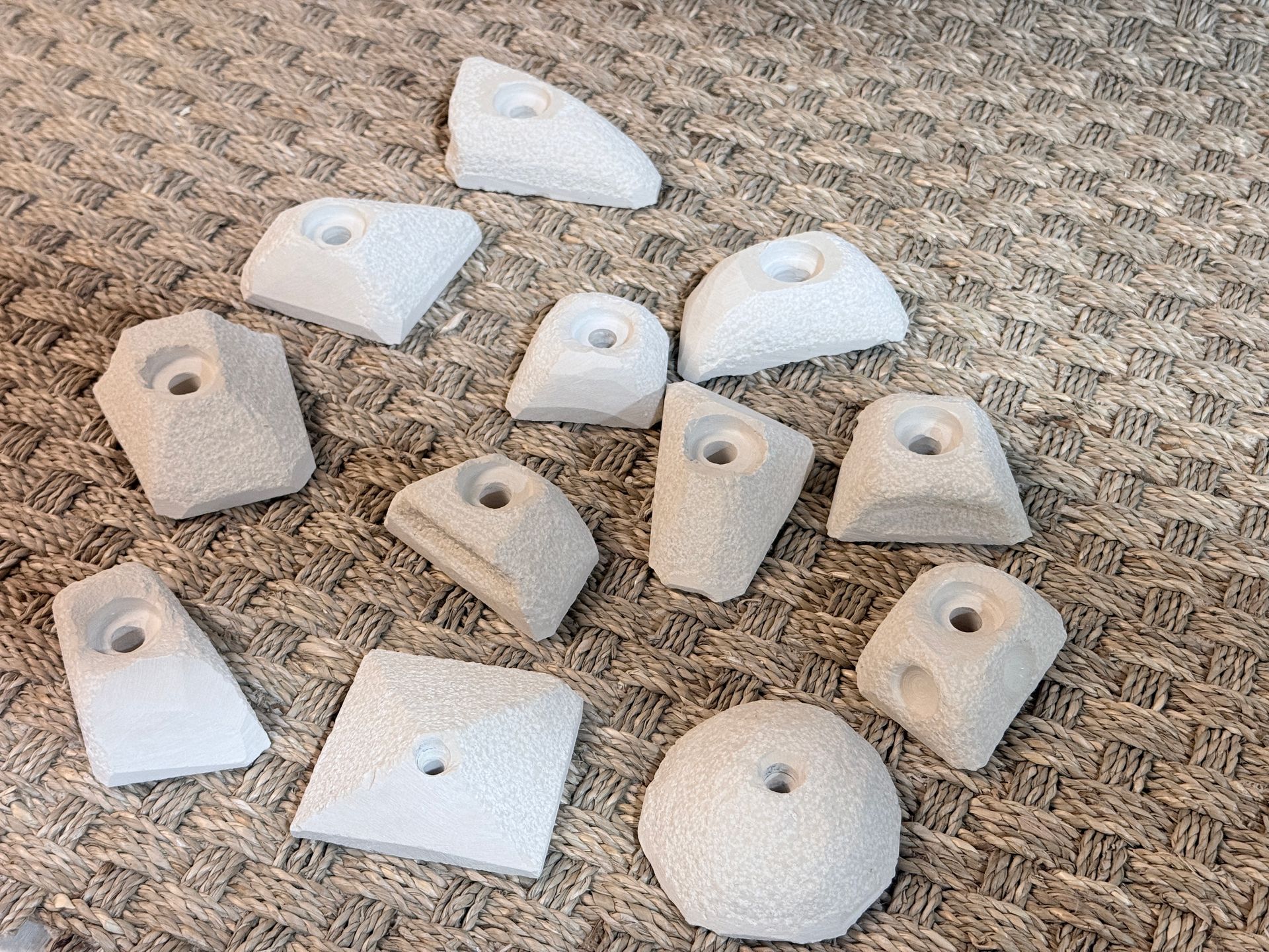 Un ensemble de prises d'escalade gris clair avec trous de fixation, disposées sur une surface texturée.