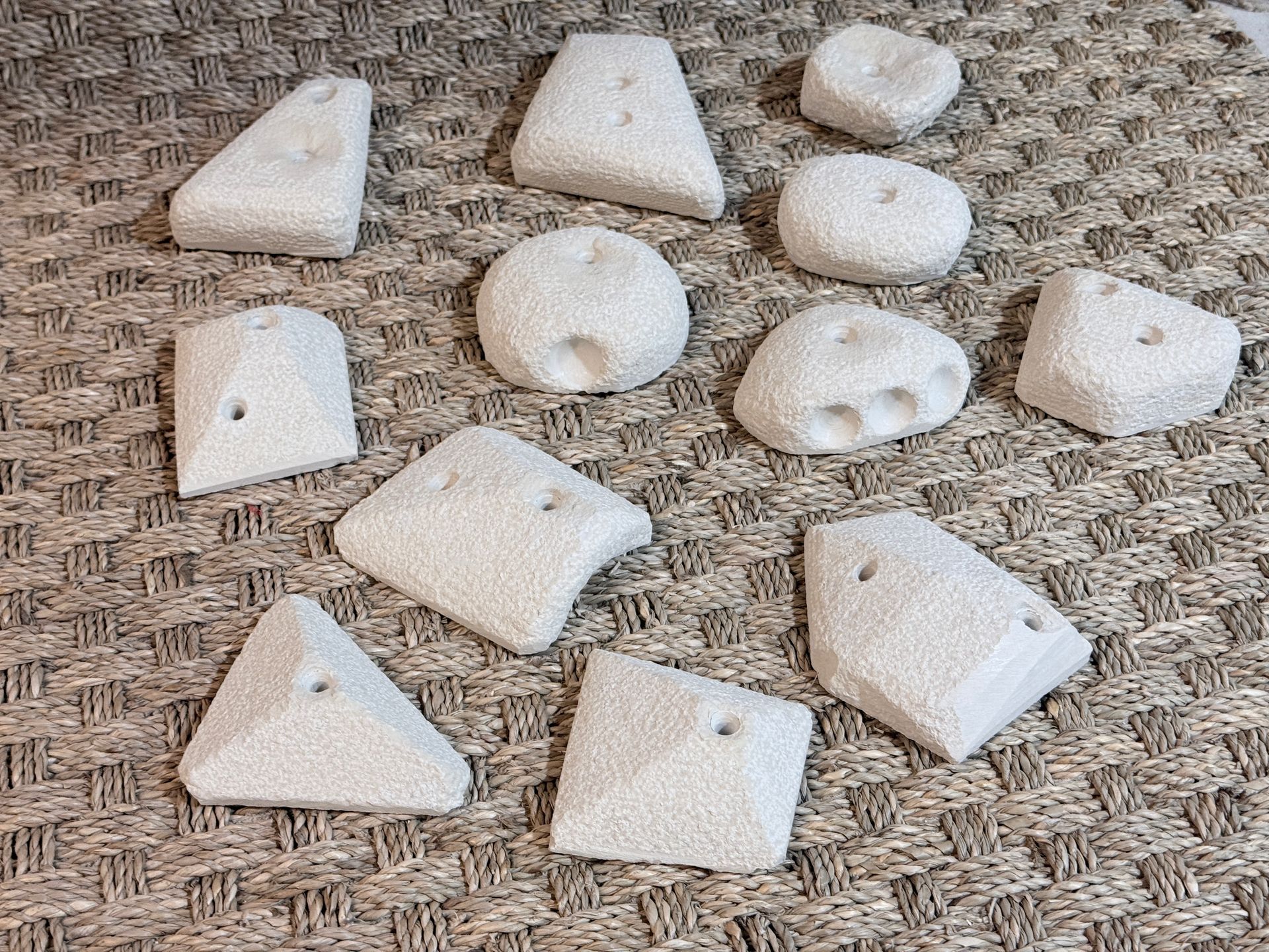 Assortiment de prises d'escalade beiges de formes variées et percées de trous, disposées sur une surface texturée.