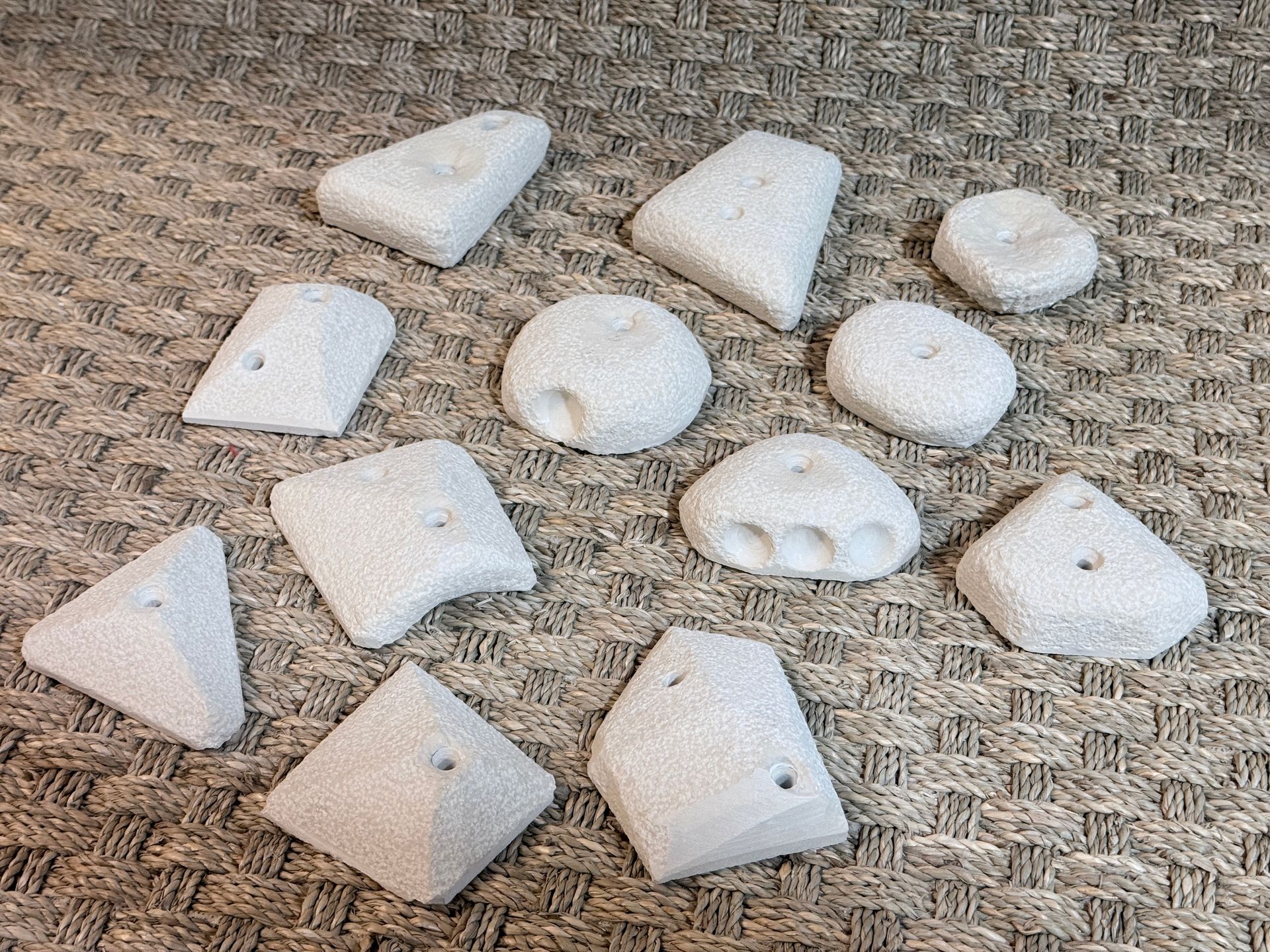 Diverses prises d'escalade de couleur claire, de formes et de textures variées, dispersées sur une surface texturée brune.