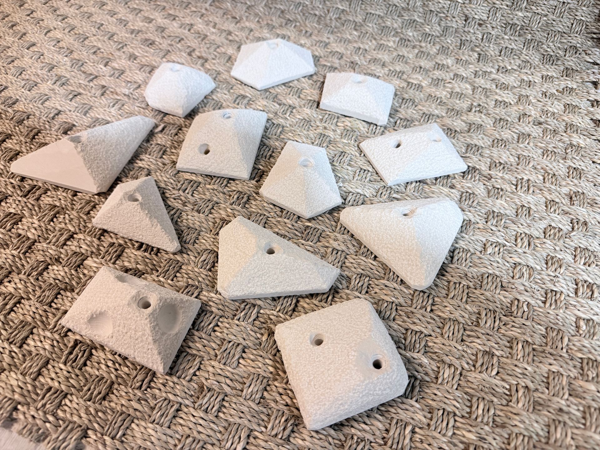 Prises d'escalade blanches dispersées sur une surface texturée de couleur neutre.