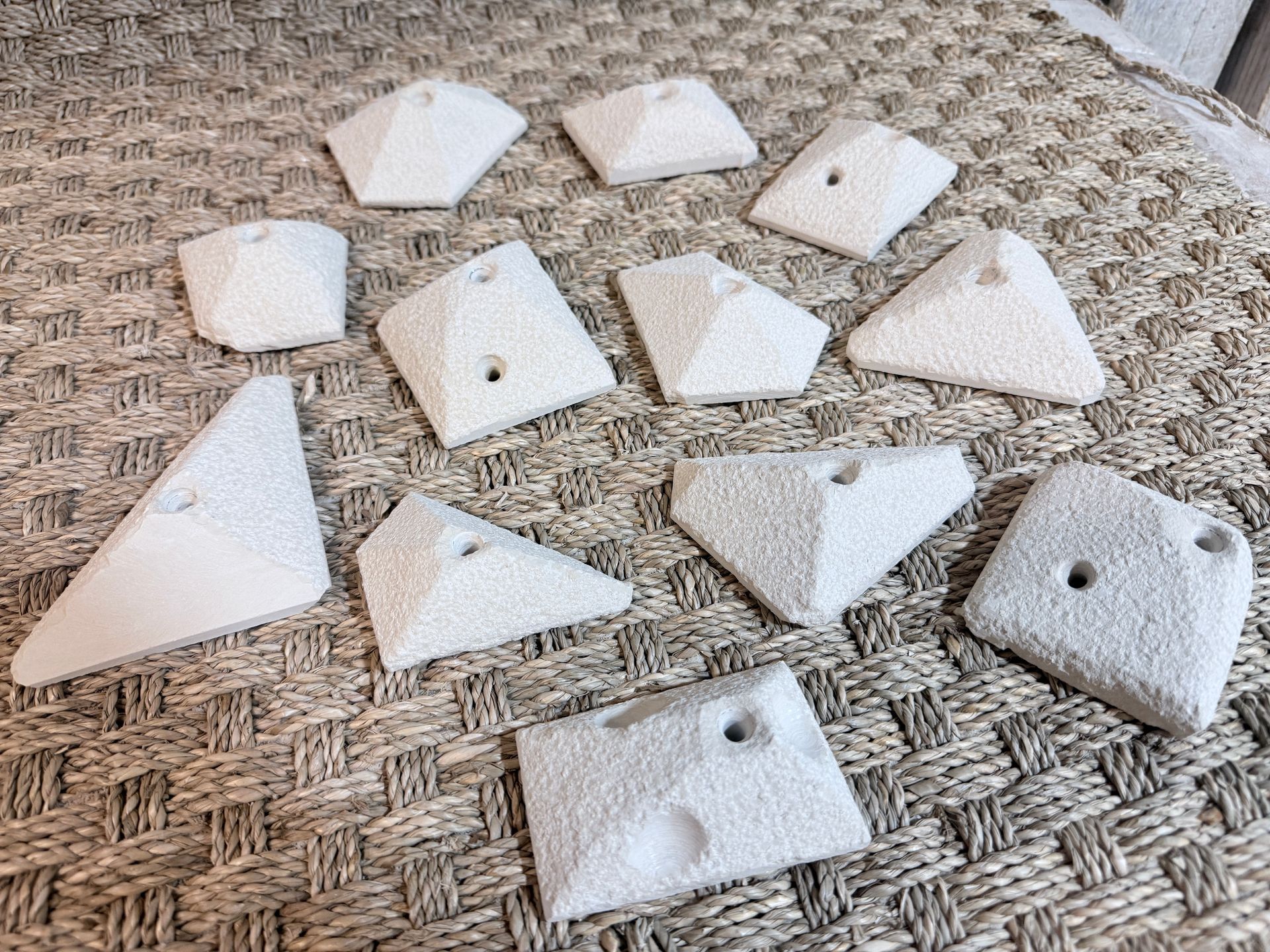 Prises d'escalade blanches disposées sur une surface texturée. Chacune est percée d'un trou pour la fixation.