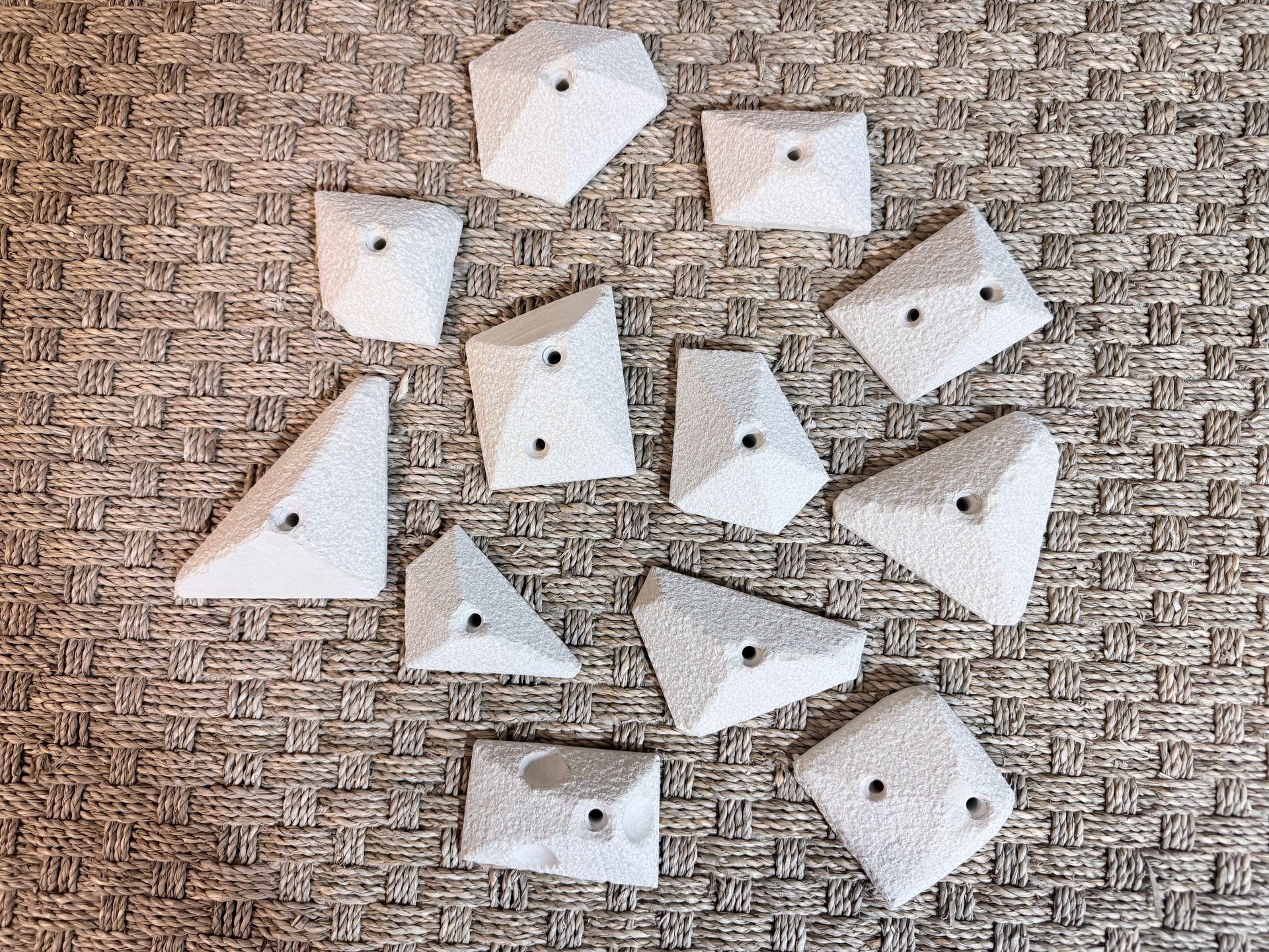 Prises d'escalade blanches de formes variées, disposées sur une surface brune texturée.