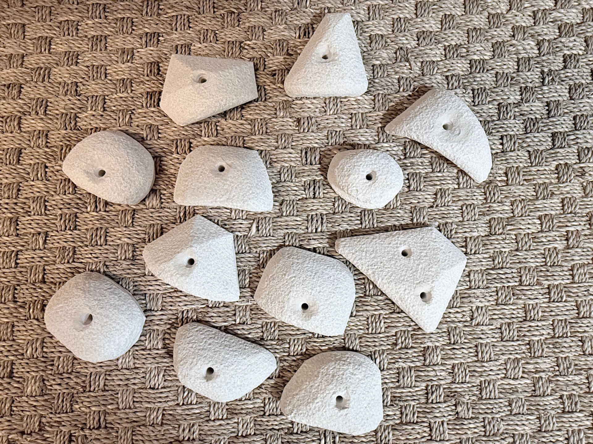 Prises d'escalade de formes et de tailles variées, gris clair, disposées sur une surface texturée brune.