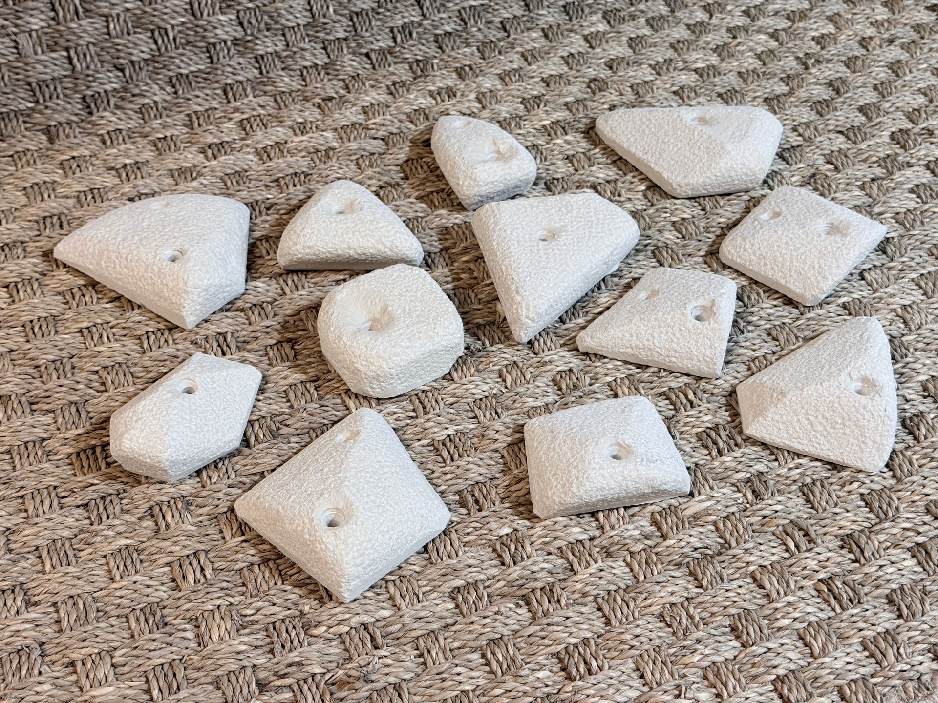 Gros plan sur une collection de prises d'escalade blanches, texturées et géométriques sur une surface brune à motifs.