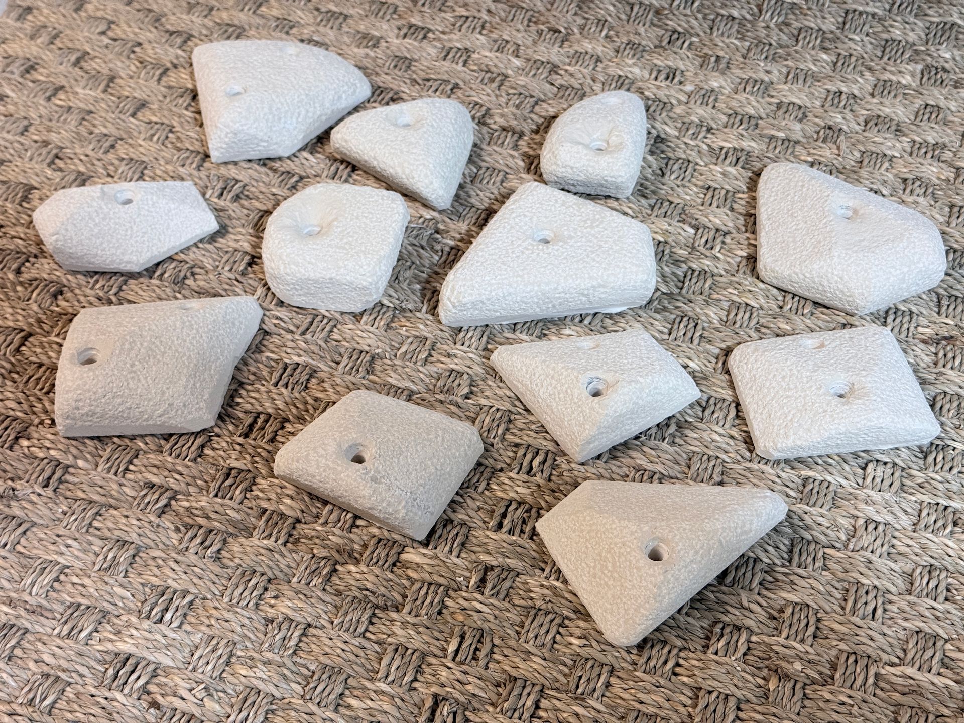 Prises d'escalade gris clair à surfaces texturées, dispersées sur une surface brune à motifs.