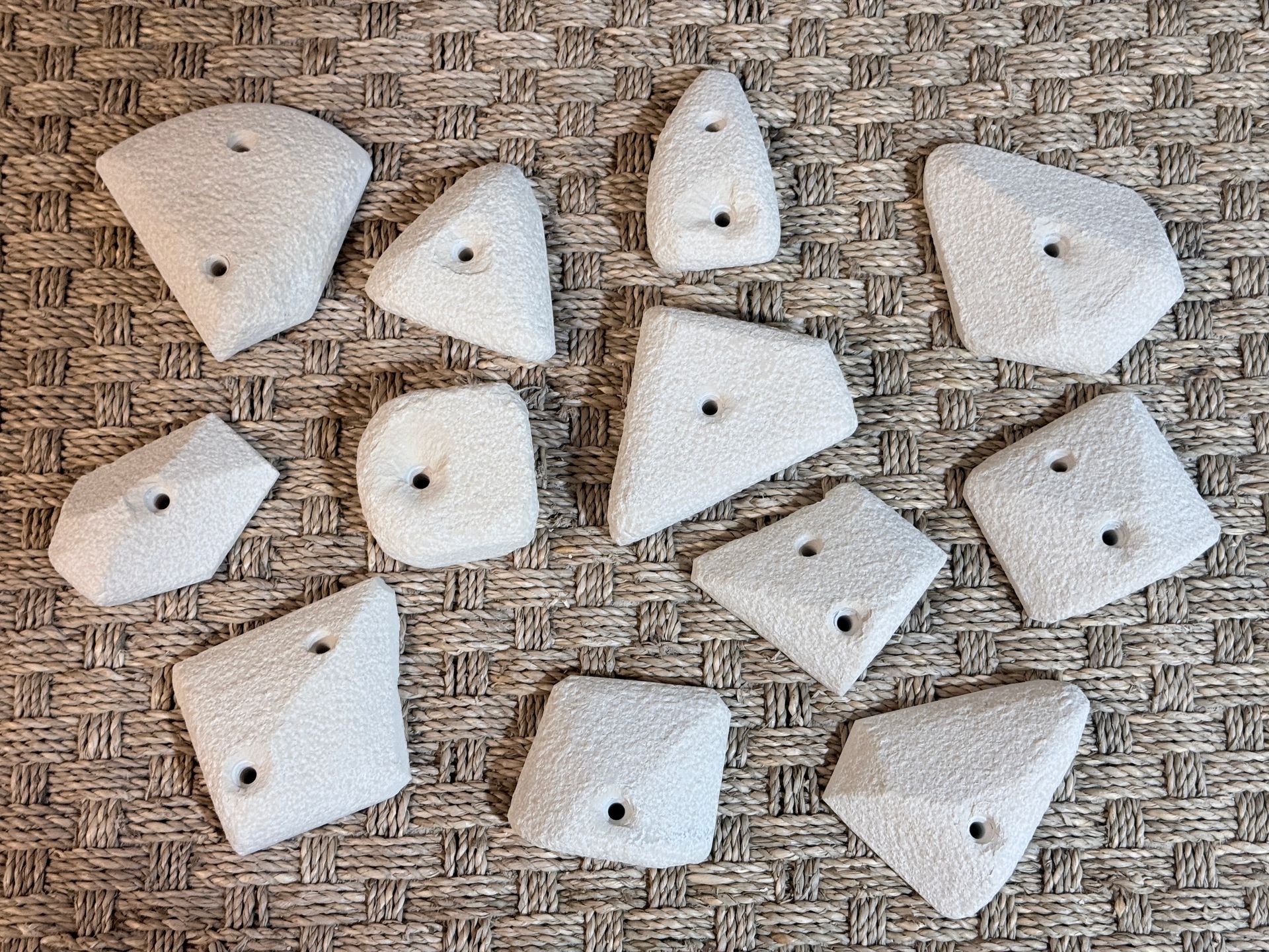 Prises d'escalade de tailles et de formes variées, disposées sur une surface texturée. Blanches, avec trous de fixation.