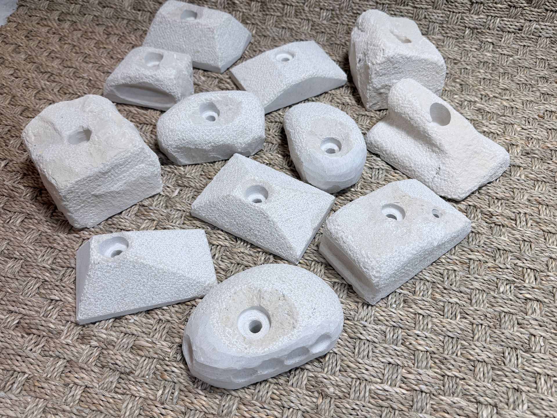 Une collection de prises d'escalade blanches à surfaces texturées, dispersées sur une surface beige.