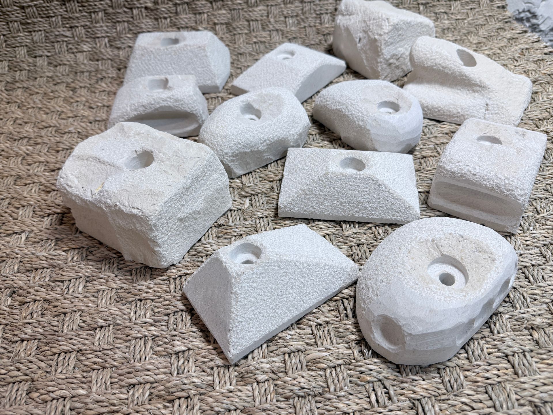 Prises d'escalade blanches avec trous centraux, disposées sur une surface brune texturée.