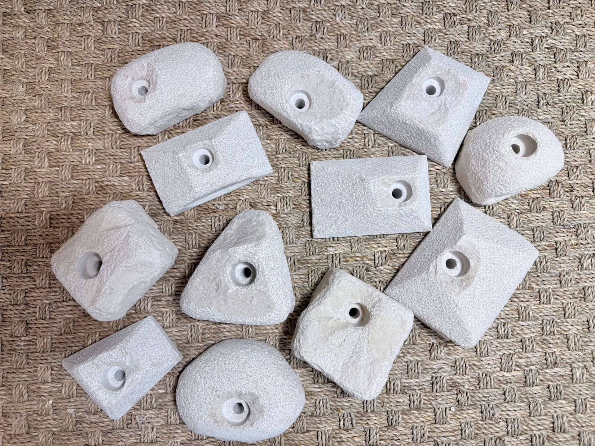 Prises d'escalade de formes et de tailles variées, gris clair, avec trous de fixation, sur une surface texturée.