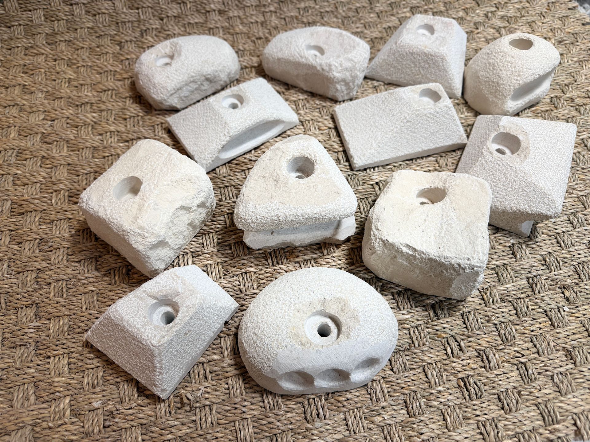 Assortiment de prises d'escalade en pierre claire et poreuse, avec trous centraux, disposées sur une surface texturée.