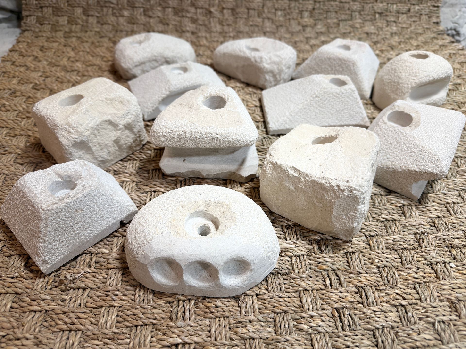 Sculptures en pierre blanche et poreuse, percées de trous centraux, disposées sur une surface texturée et tissée.