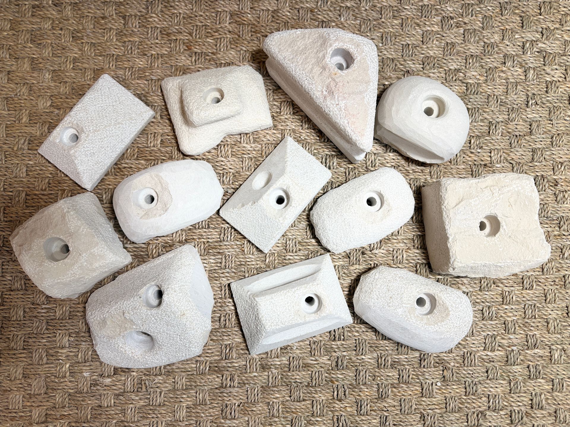 Des prises d'escalade blanches sont dispersées sur une surface brune texturée, chacune comportant un trou central.