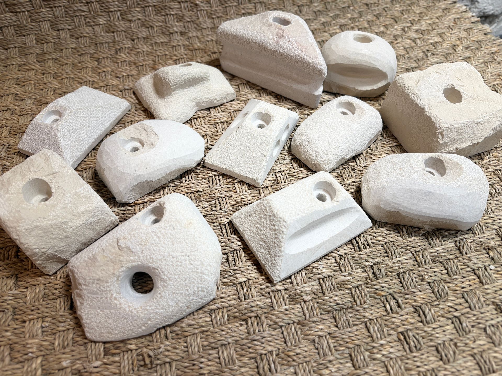Collection de prises d'escalade blanc cassé, de formes variées, avec des trous pré-percés, sur une surface texturée.