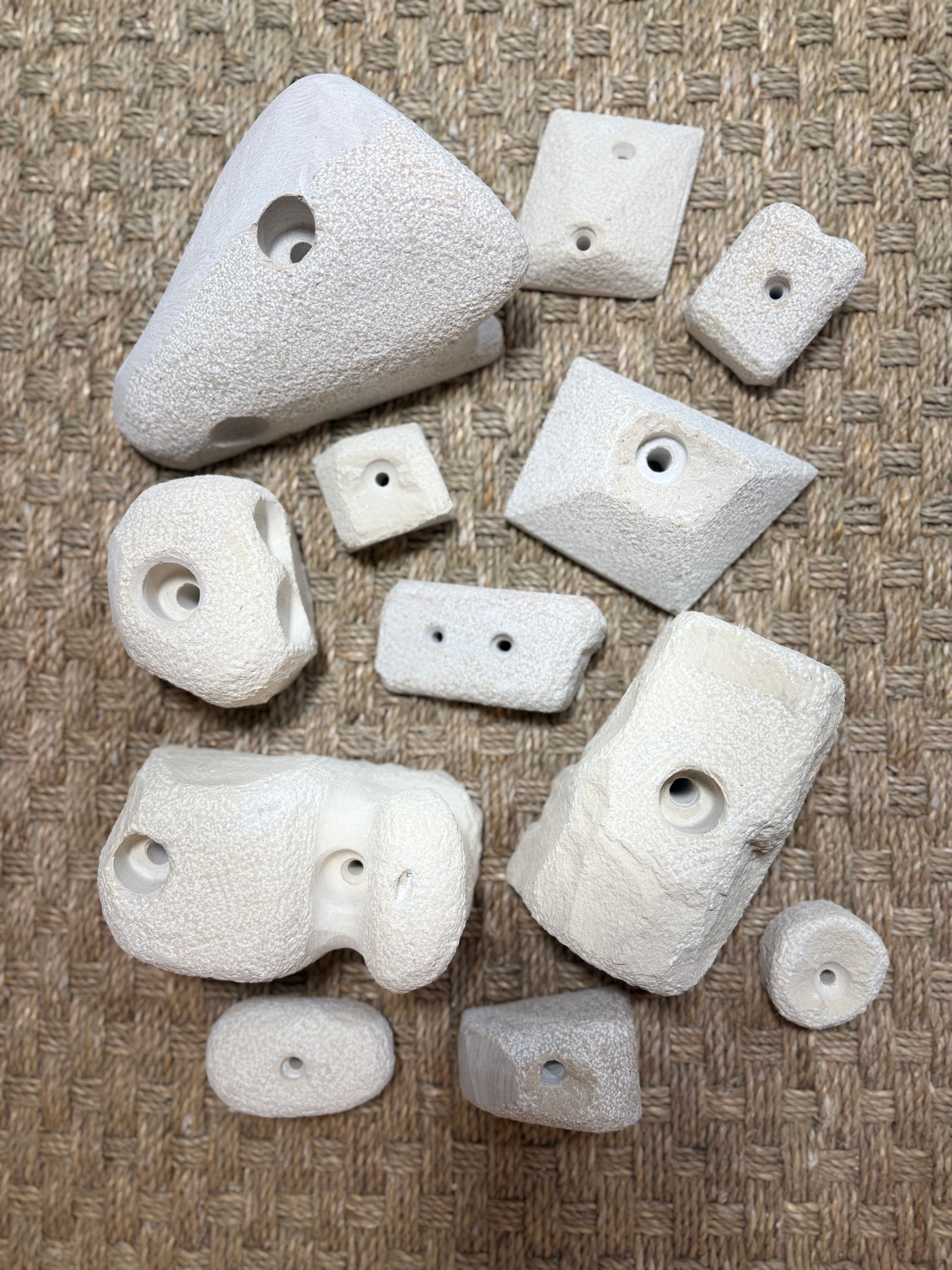 Diverses prises d'escalade de couleur claire, munies de trous de fixation, sont dispersées sur une surface texturée.