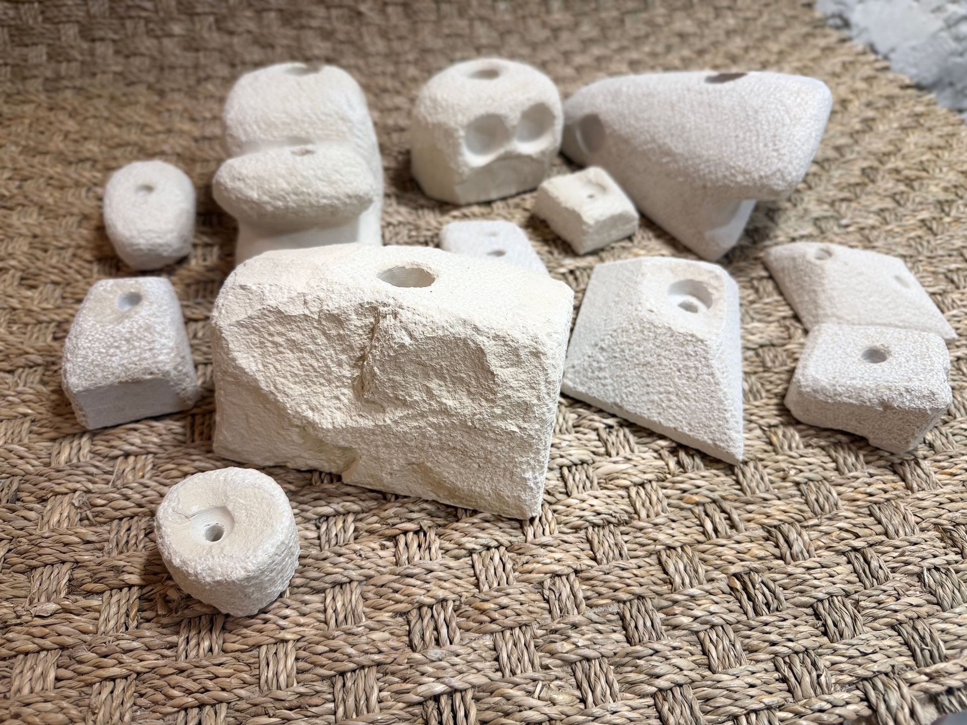 Gros plan sur plusieurs prises d'escalade blanches et texturées, de formes variées, sur un tapis tissé.