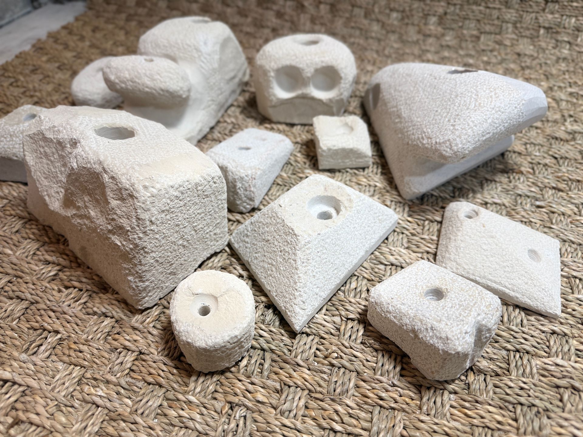 Assortiment de prises d'escalade blanc cassé sur une surface texturée et tissée. Certaines prises sont percées de trous.