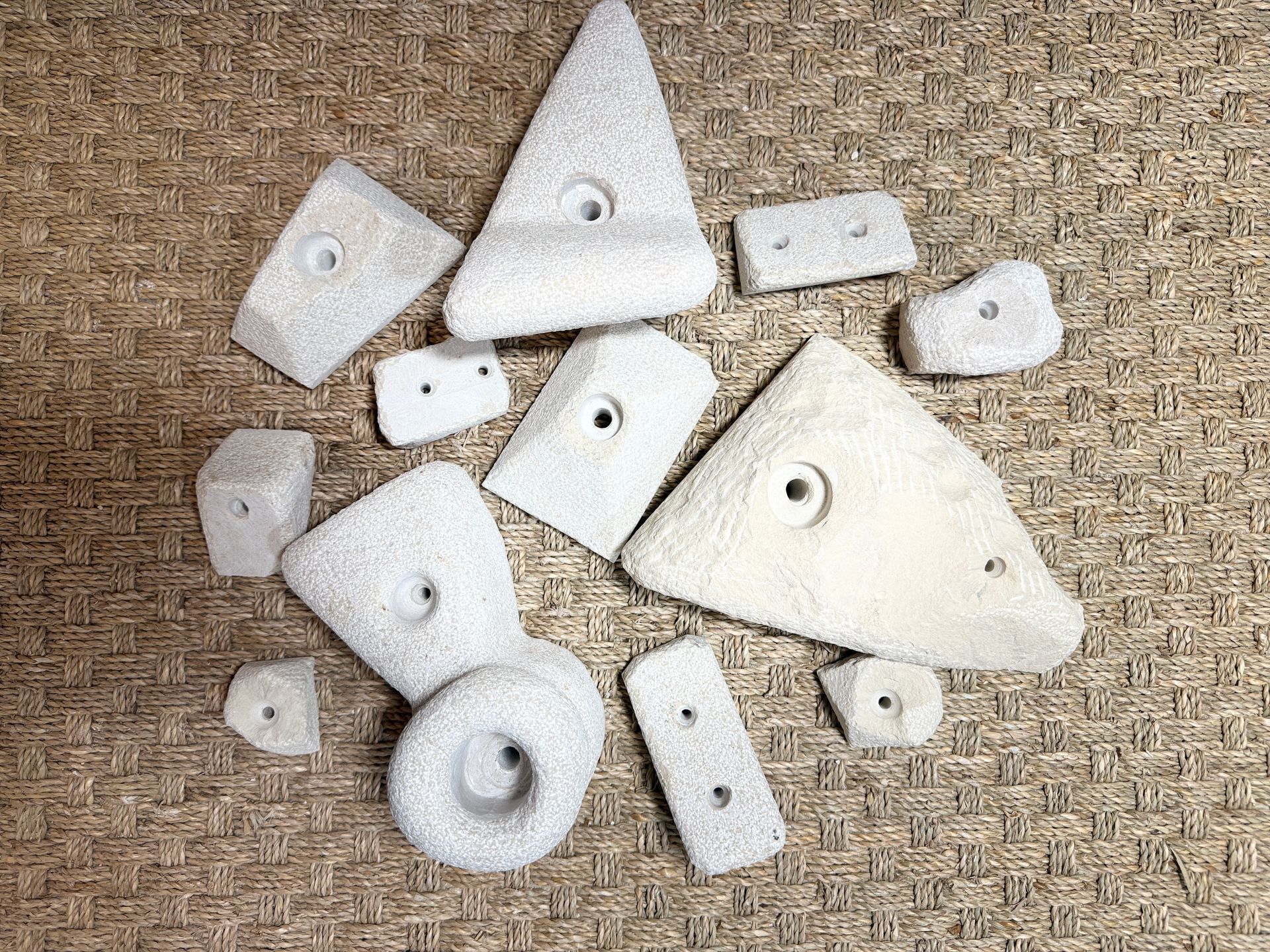 Prises d'escalade, de formes et de tailles variées, blanc cassé, disposées sur une surface texturée brune.