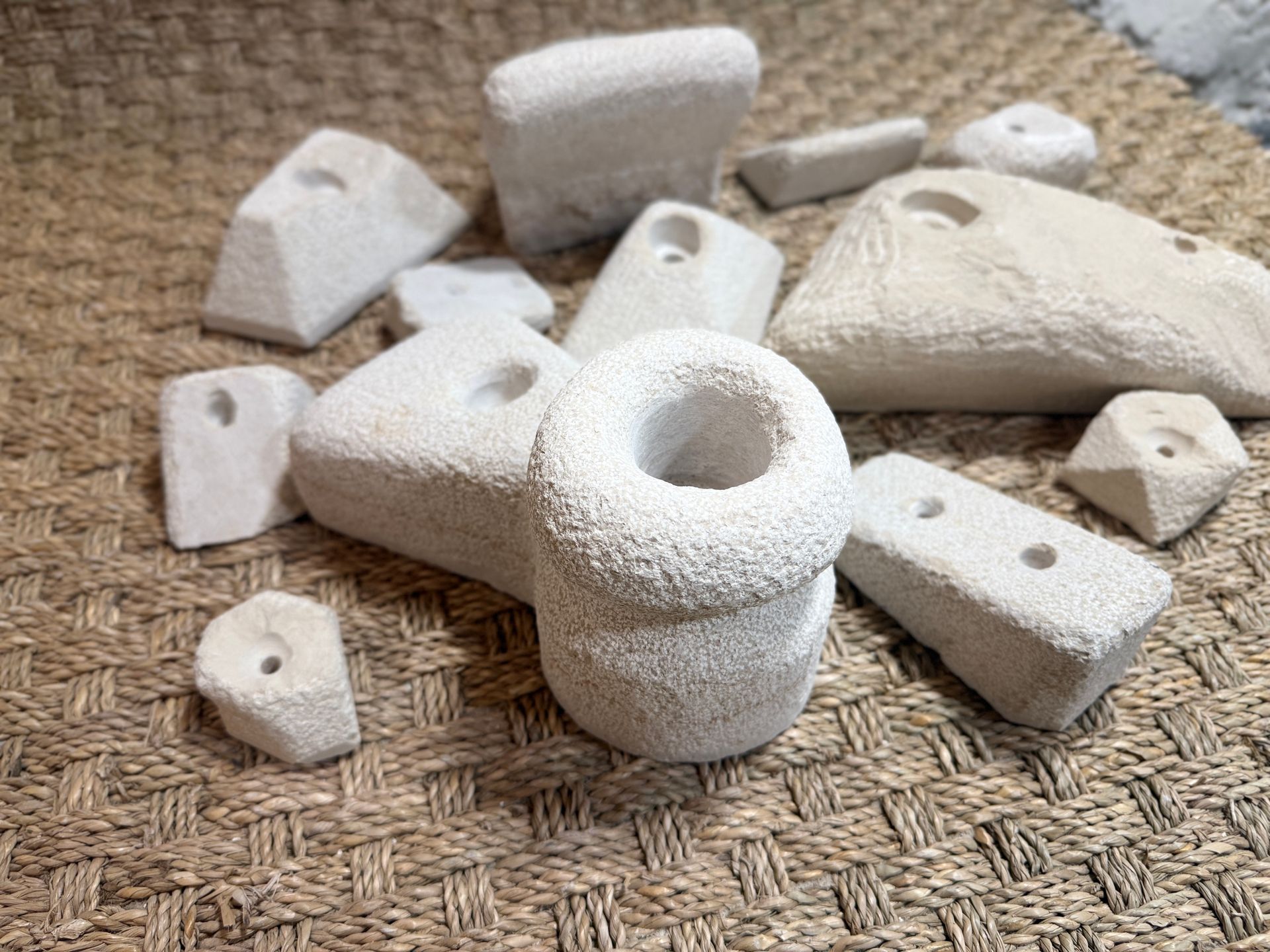 Prises d'escalade blanches de formes et de textures variées, disposées sur un tapis tissé.
