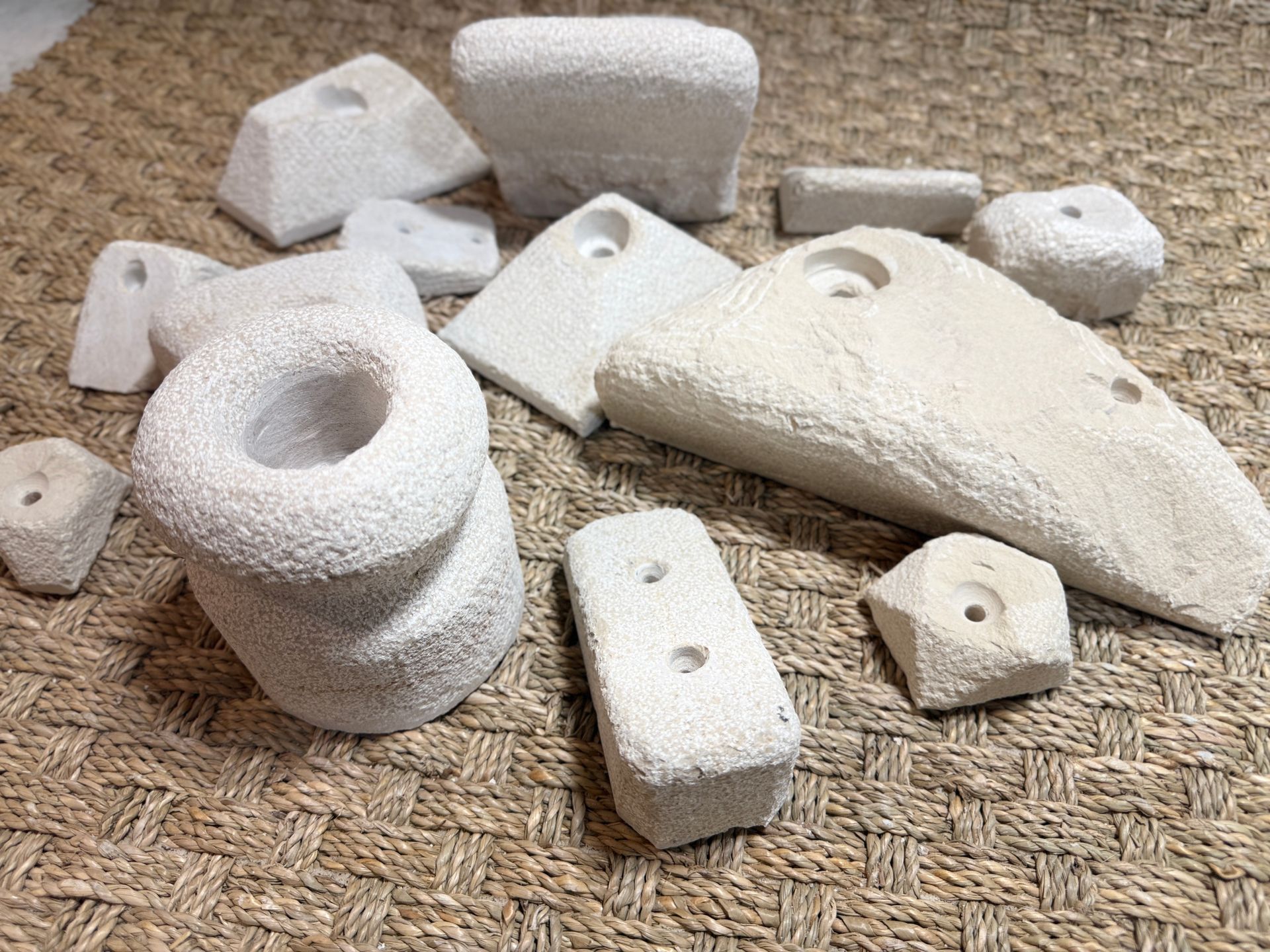 Assortiment de prises d'escalade blanches et poreuses dispersées sur une surface tissée beige.