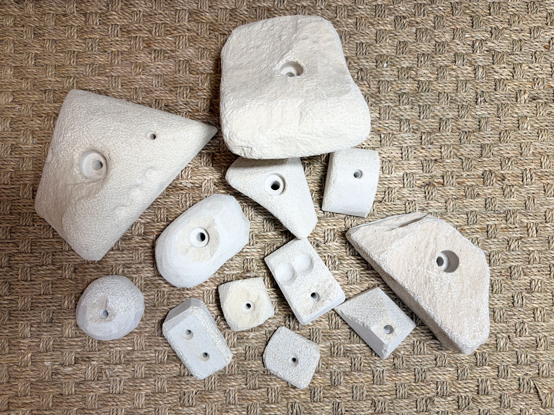 Des prises d'escalade blanc cassé de formes et de tailles variées, dispersées sur un tapis en osier.