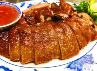 Gebratene Entenscheiben, serviert auf einem gemusterten Teller mit roter Dip-Sauce und Kräutergarnitur.