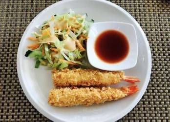 Zwei goldbraun frittierte Garnelen-Tempura, serviert mit einem Beilagensalat aus geraspeltem Gemüse und einer kleinen Schüssel Dip-Sauce.