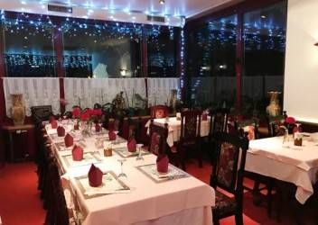 Esszimmer mit zum Abendessen gedeckten Tischen, mit weissen Tischdecken, roten Servietten, Stühlen und festlicher Fensterbeleuchtung.